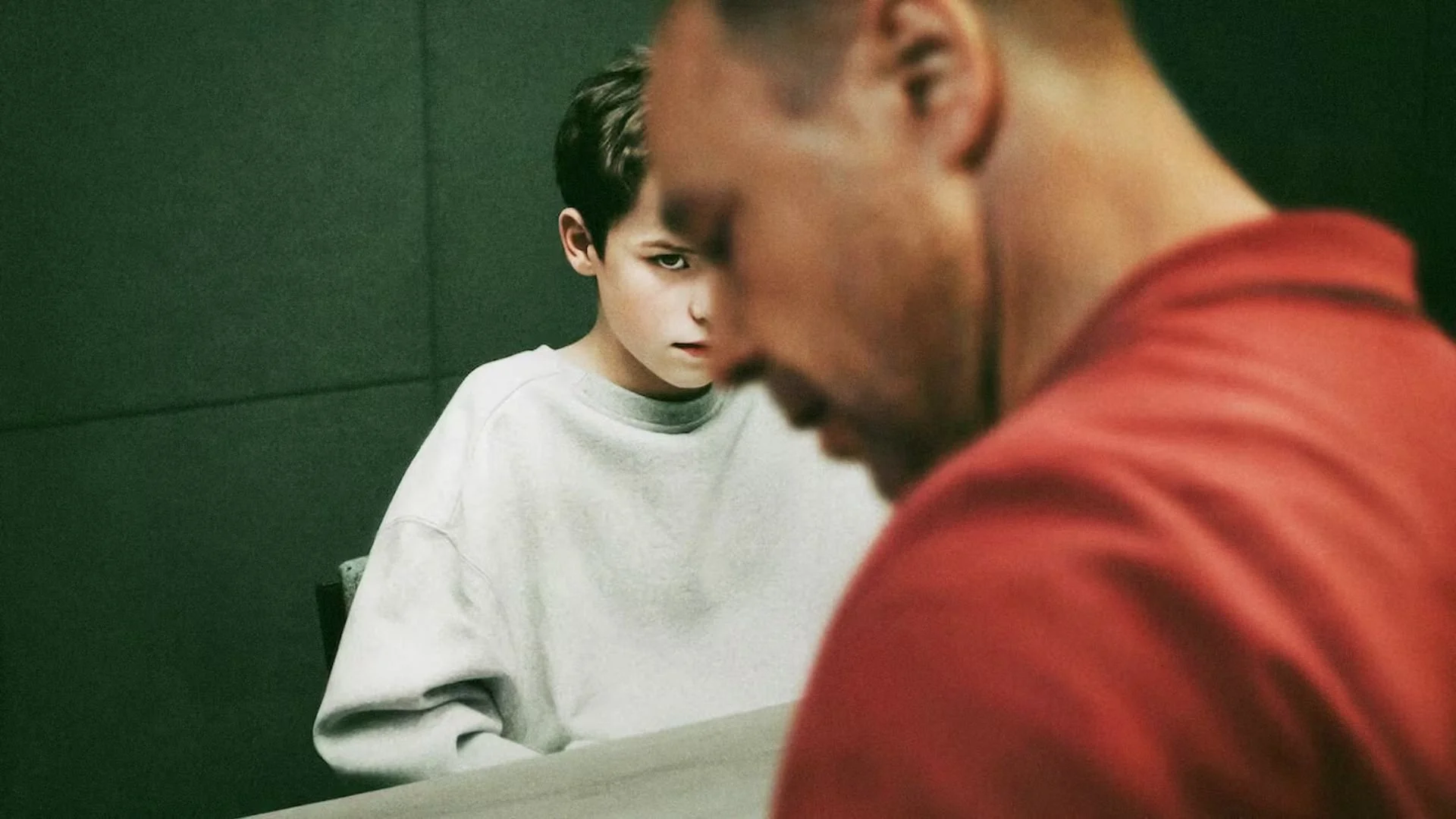 A young boy sitting in a police cell with his anguished father looking on