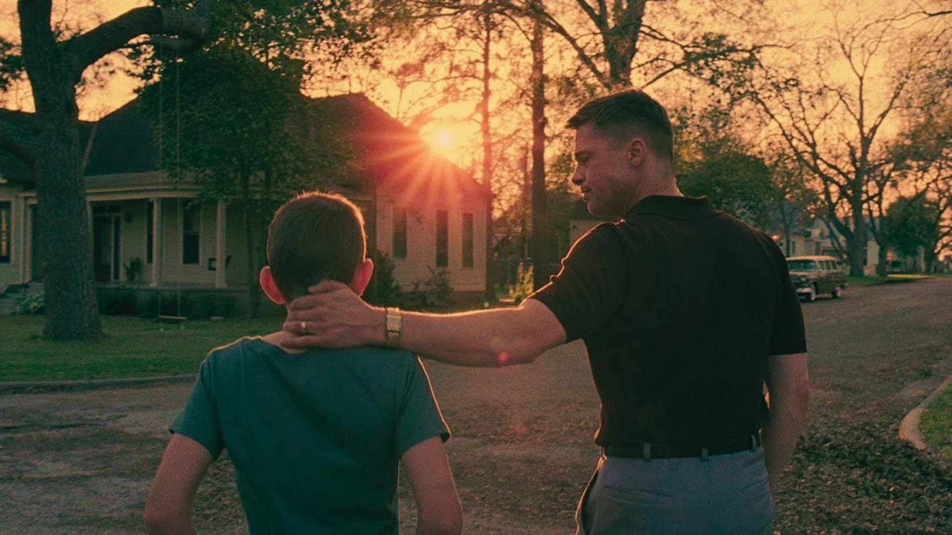 A father with his arm around his son as the sun sets
