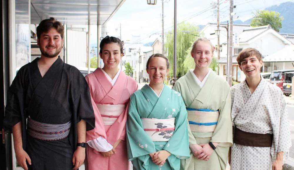 Five people standing side by side outdoors, all dressed in traditional Japanese kimonos, smiling for the camera.