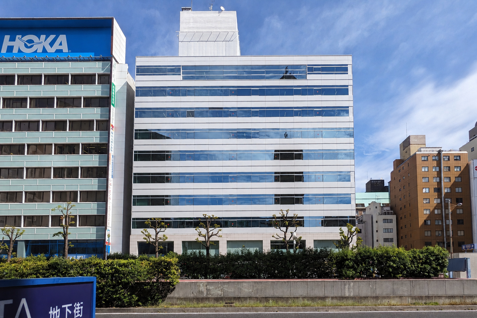 A cityscape with a modern glass office building and neighboring high-rise buildings under a blue sky with some clouds.