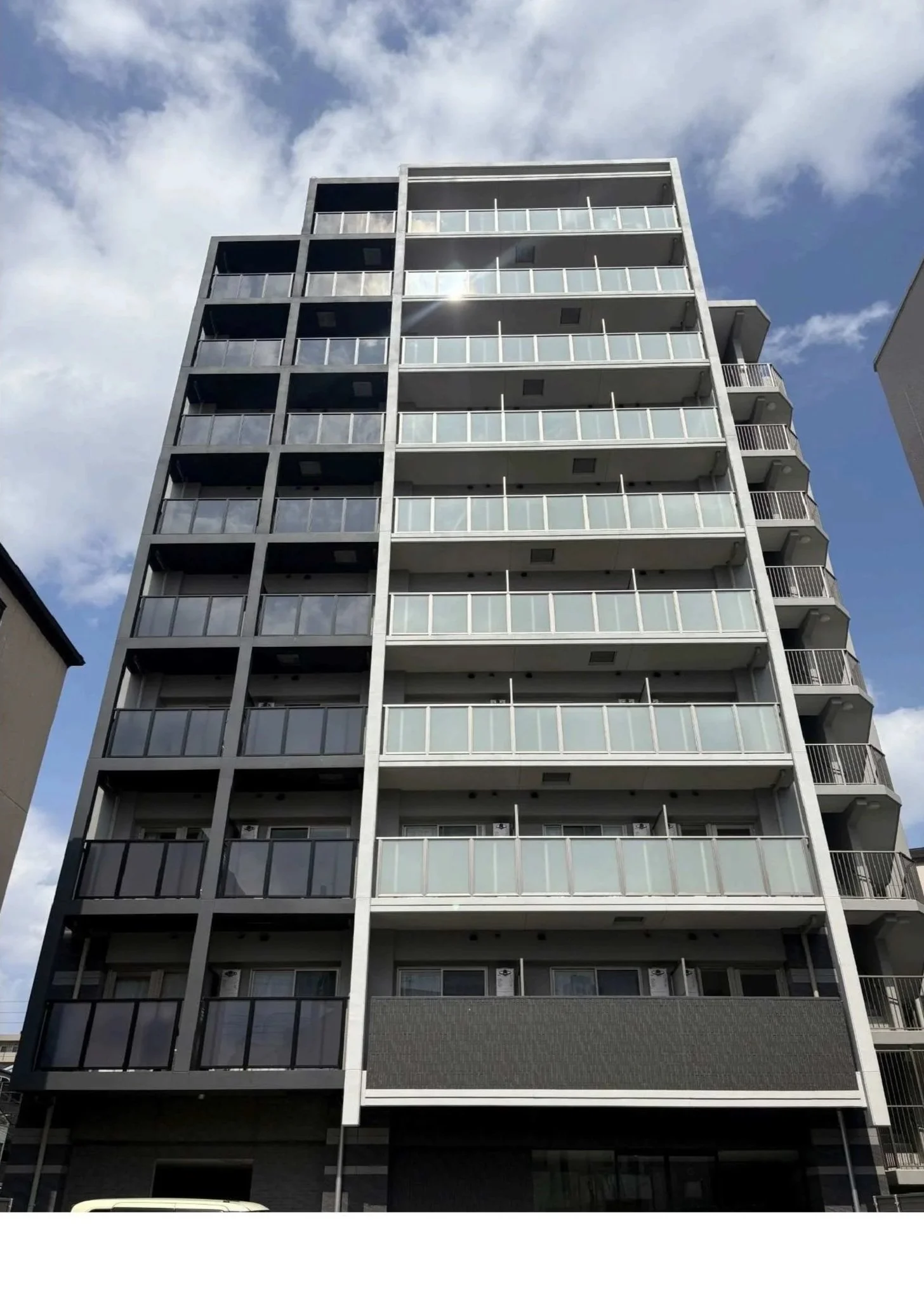 Modern multi-story apartment building with balconies and glass railings under a partly cloudy sky.