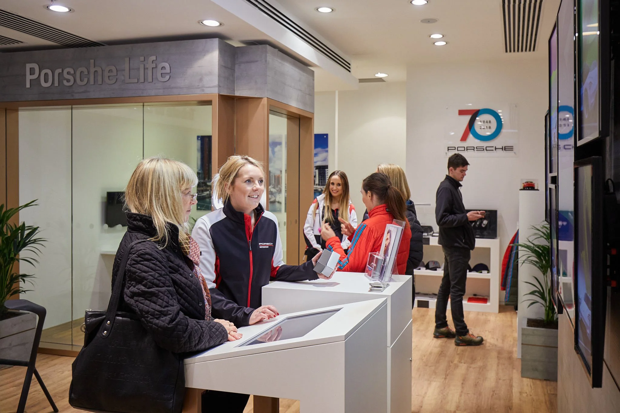 ambassador with customer at Porsche retail pop up store in the UK engaging and smiling during the temporary car retail shop
