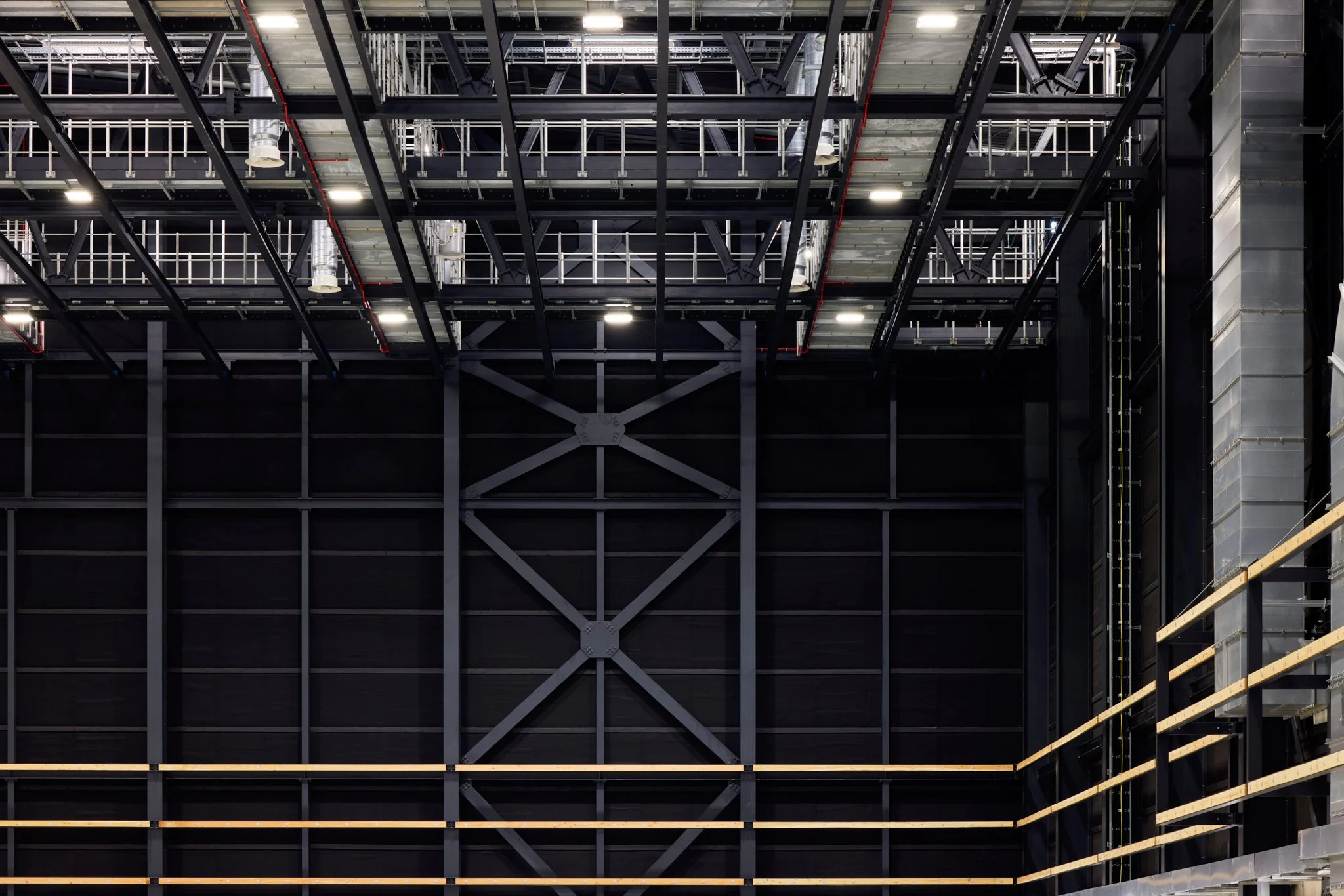 Interior of a large industrial or commercial building under construction with metal framework, scaffolding, and staircase.