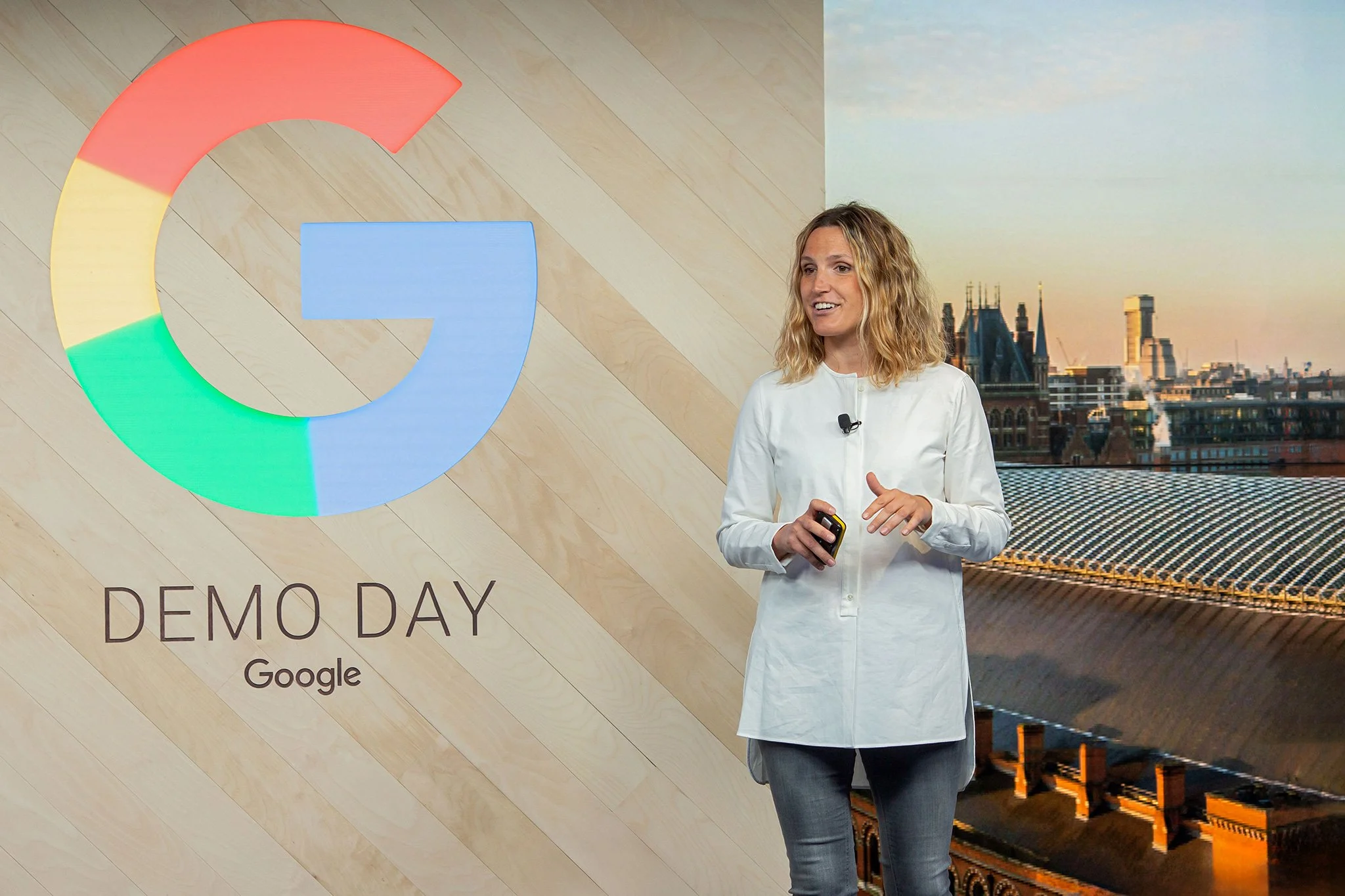Google Demo Day Event with host on stage next to a large G and lcd screen with London skyline