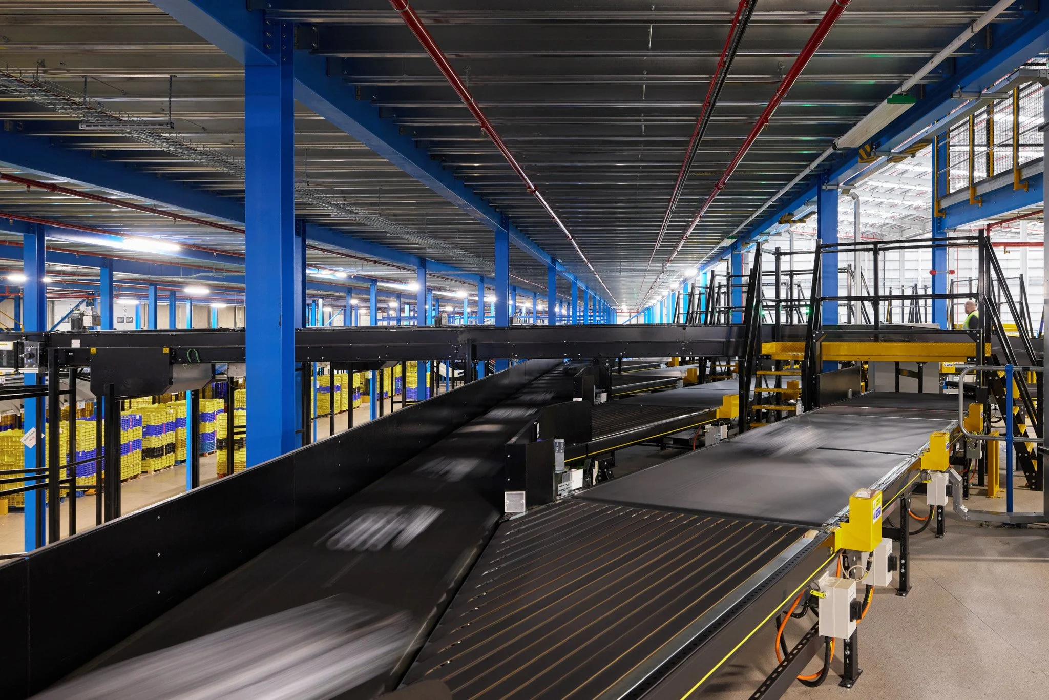 Inside an industrial warehouse with blue support beams and conveyor belts for sorting packages.