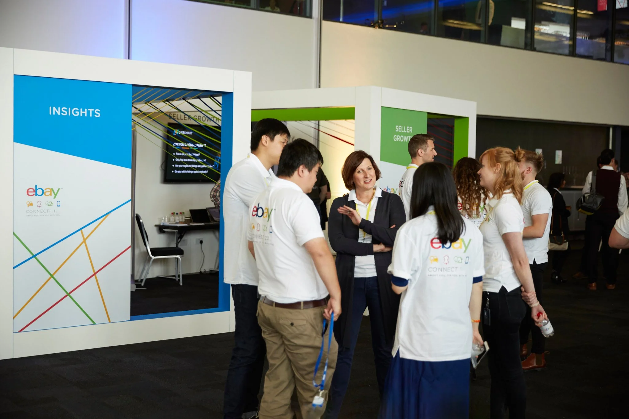 Group of people engaging in conversation at a eBay conference or event, with eBay branding and signage visible.