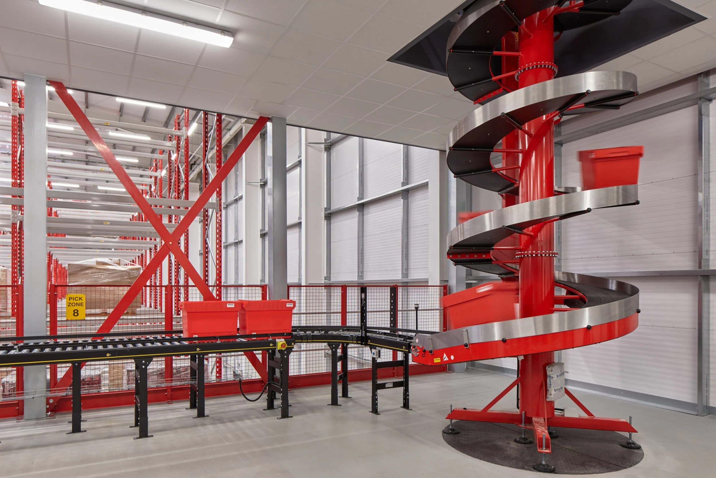 An indoor warehouse or storage facility with a red spiral conveyor, metal shelving units, and a section marked 'PICK ZONE 8'.