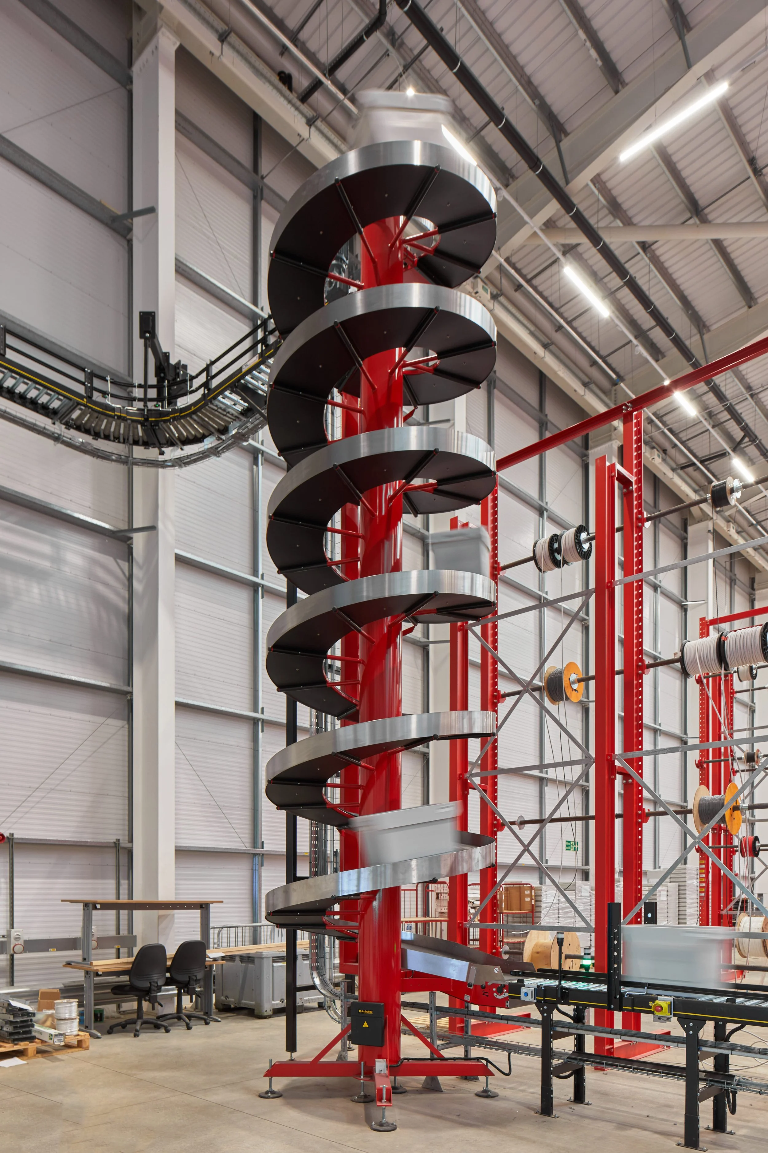 Large spiral slide inside a factory or industrial building with high ceiling, steel beams, and various equipment.