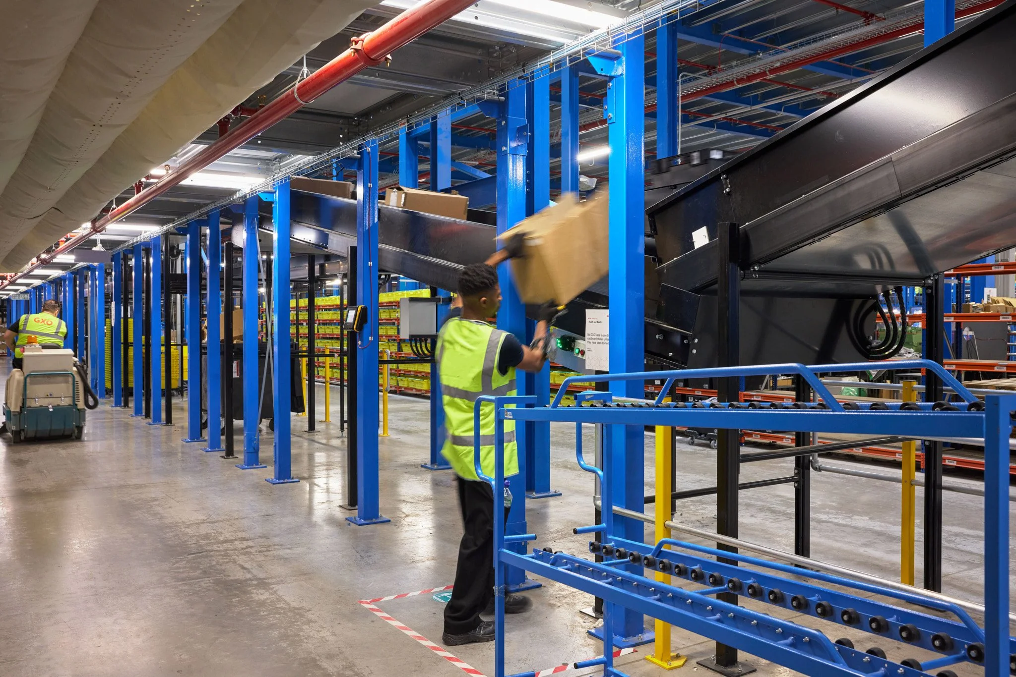 Workers in a warehouse operate conveyor belts and handling equipment for sorting packages.