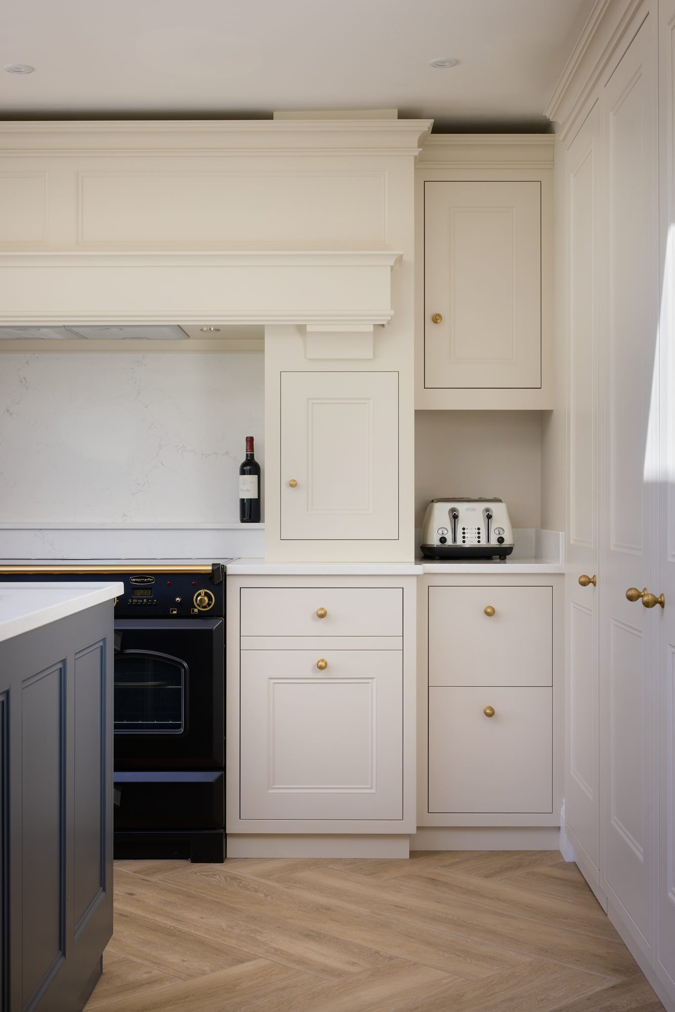 A kitchen with white cabinetry, a wine bottle on the countertop, a built-in oven, a toaster, and wood flooring.