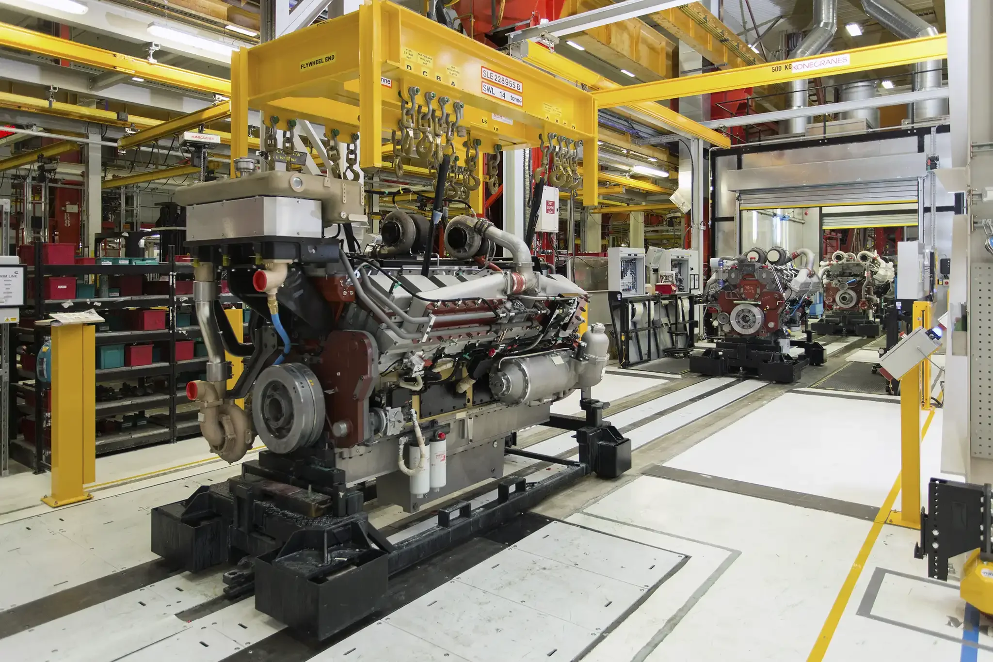 Industrial setting with machinery, yellow overhead crane, and robotic equipment, likely for manufacturing or assembly.