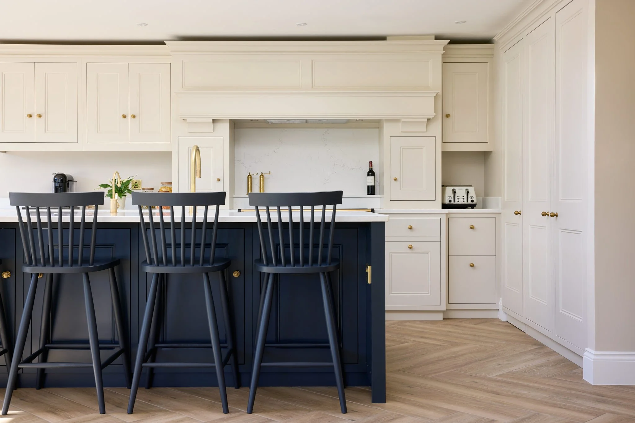 Modern kitchen with white cabinets, a dark blue island, black chairs, a gold faucet, and small appliances on the counter.