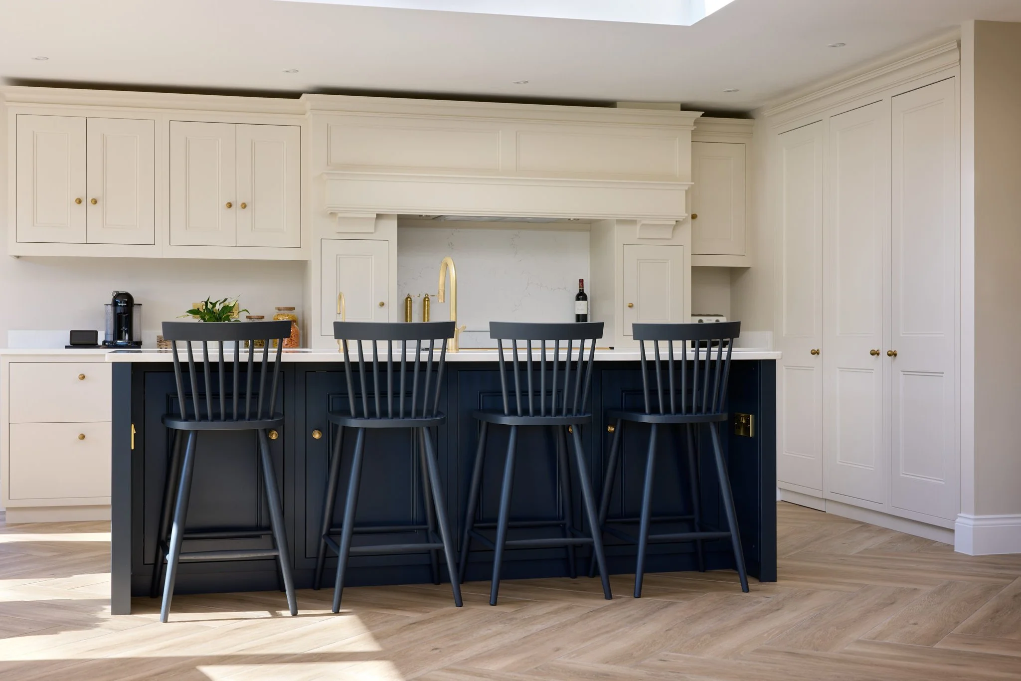 Modern kitchen with white cabinets, a navy blue island, black chairs, and a light wood floor.