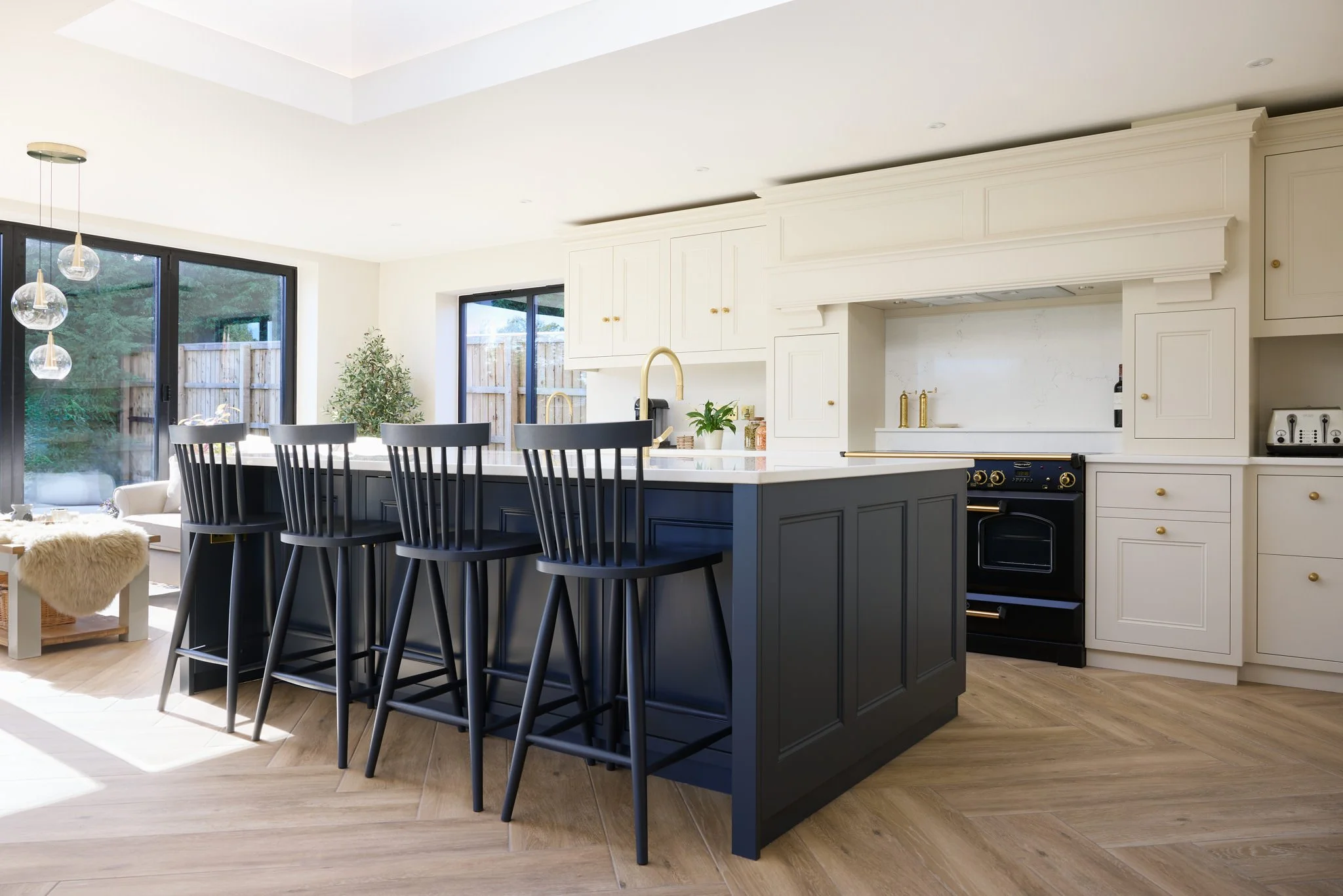 Modern kitchen with white cabinets, a navy blue island, black chairs, large windows, and hardwood floors.