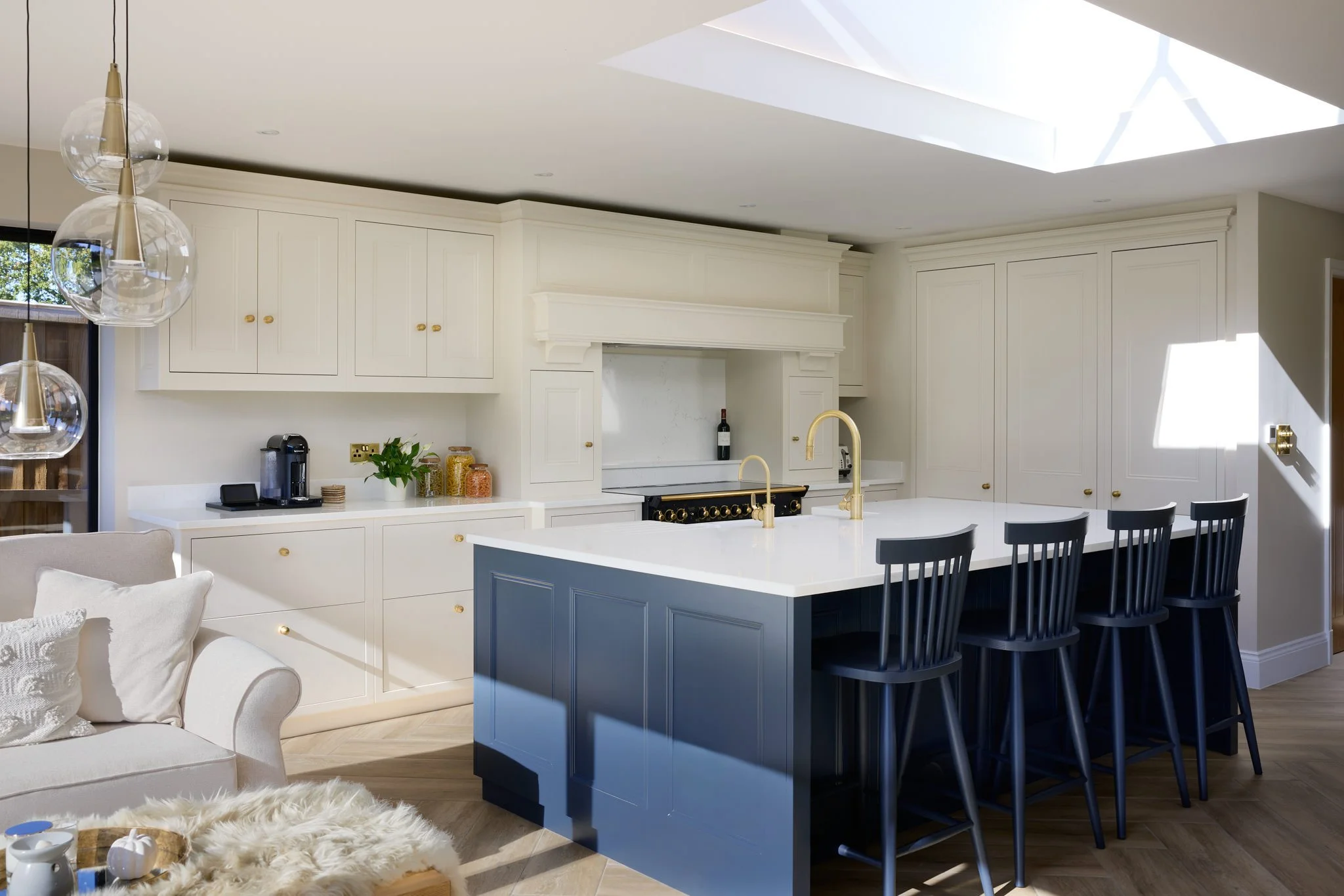 Modern kitchen with white cabinets, a dark blue island with matching chairs, and a skylight overhead. Pendant lights hang above the island.