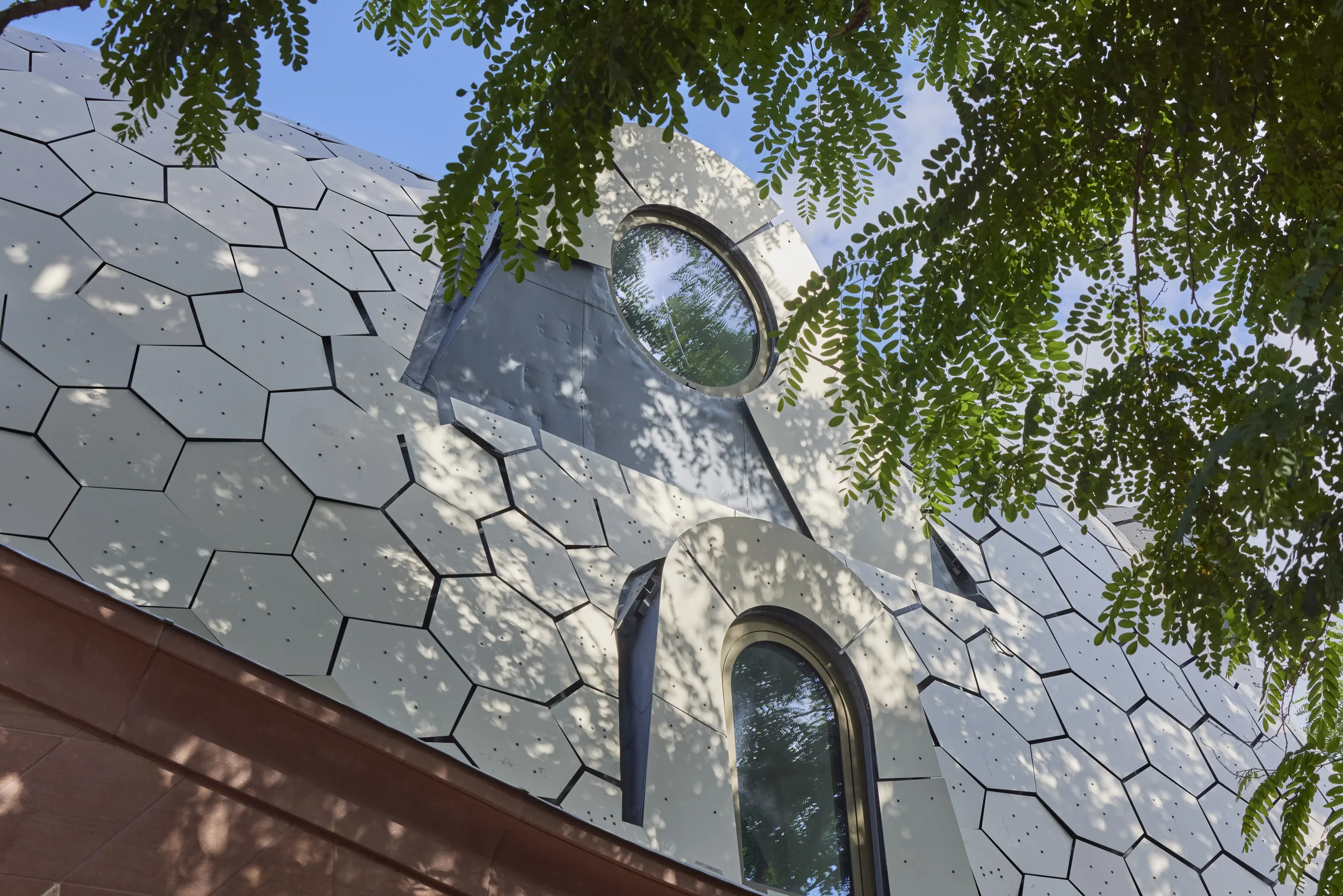 Modern building with a honeycomb patterned facade, round windows, and lush green foliage overhead.