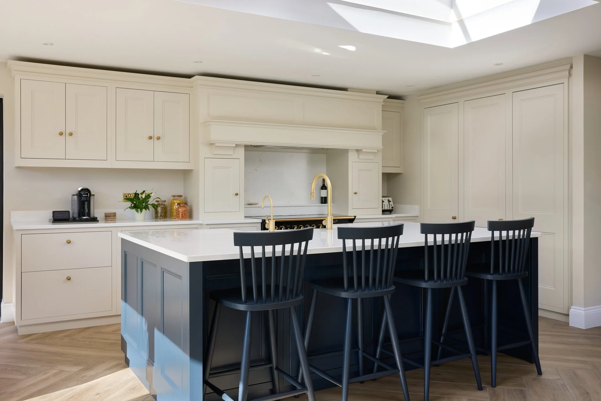 Modern kitchen with white cabinets, a white countertop, and a central kitchen island painted in navy blue with a white countertop. Five black chairs are at the island. The backsplash is white marble and provides a clean, sleek look. The ceiling has r