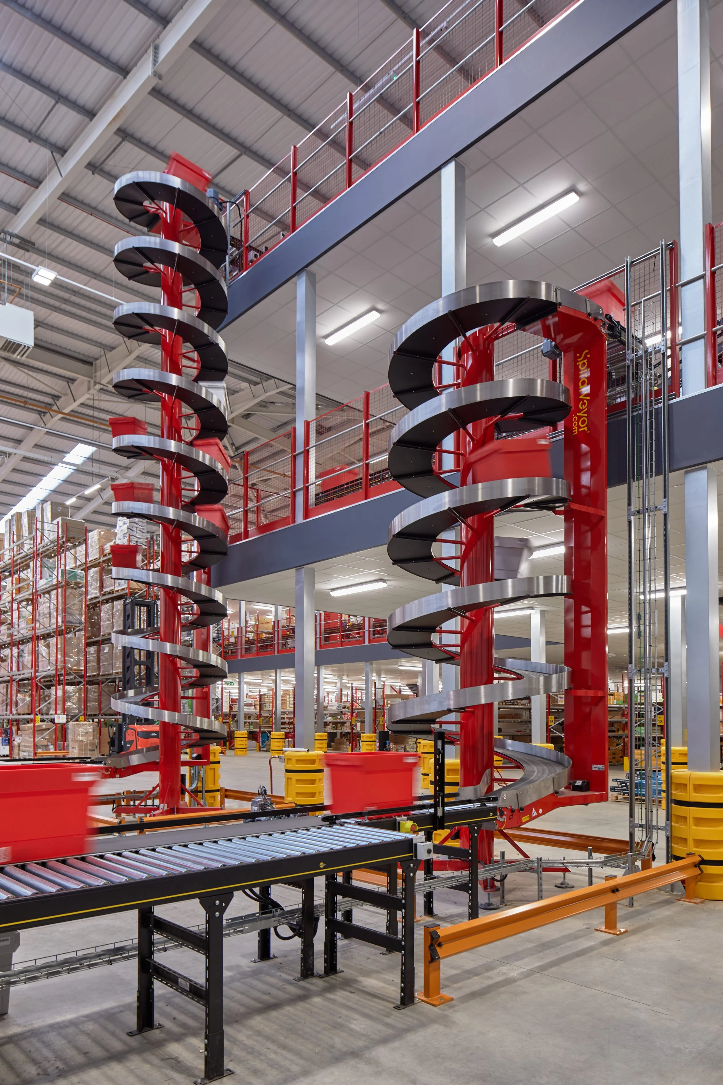 Indoor warehouse with a spiral conveyor system and shelving units filled with boxes.
