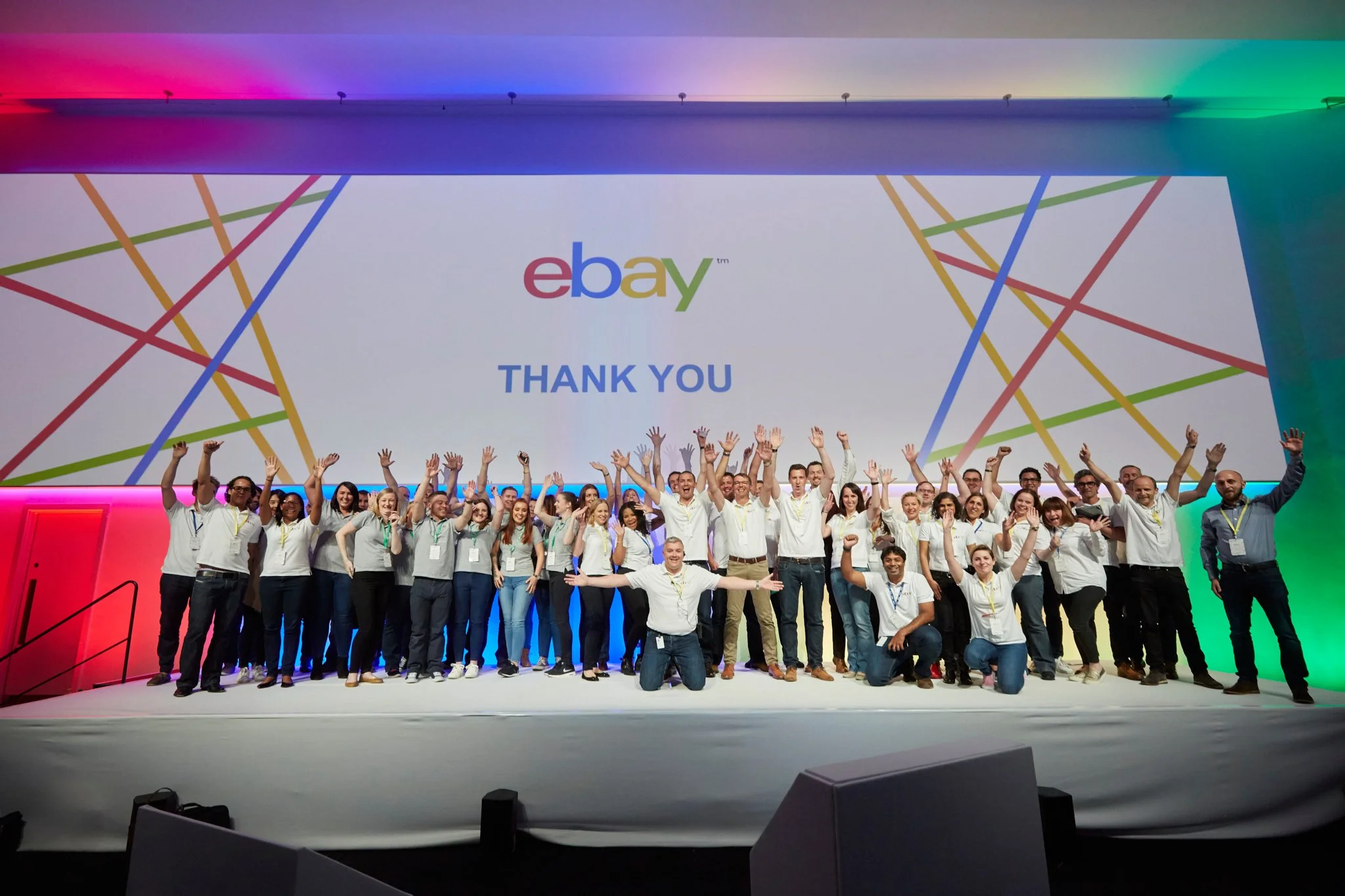 Group of people on stage at eBay event, waving and smiling, with a large screen behind them displaying the eBay logo and 'THANK YOU' message, colorful lighting.