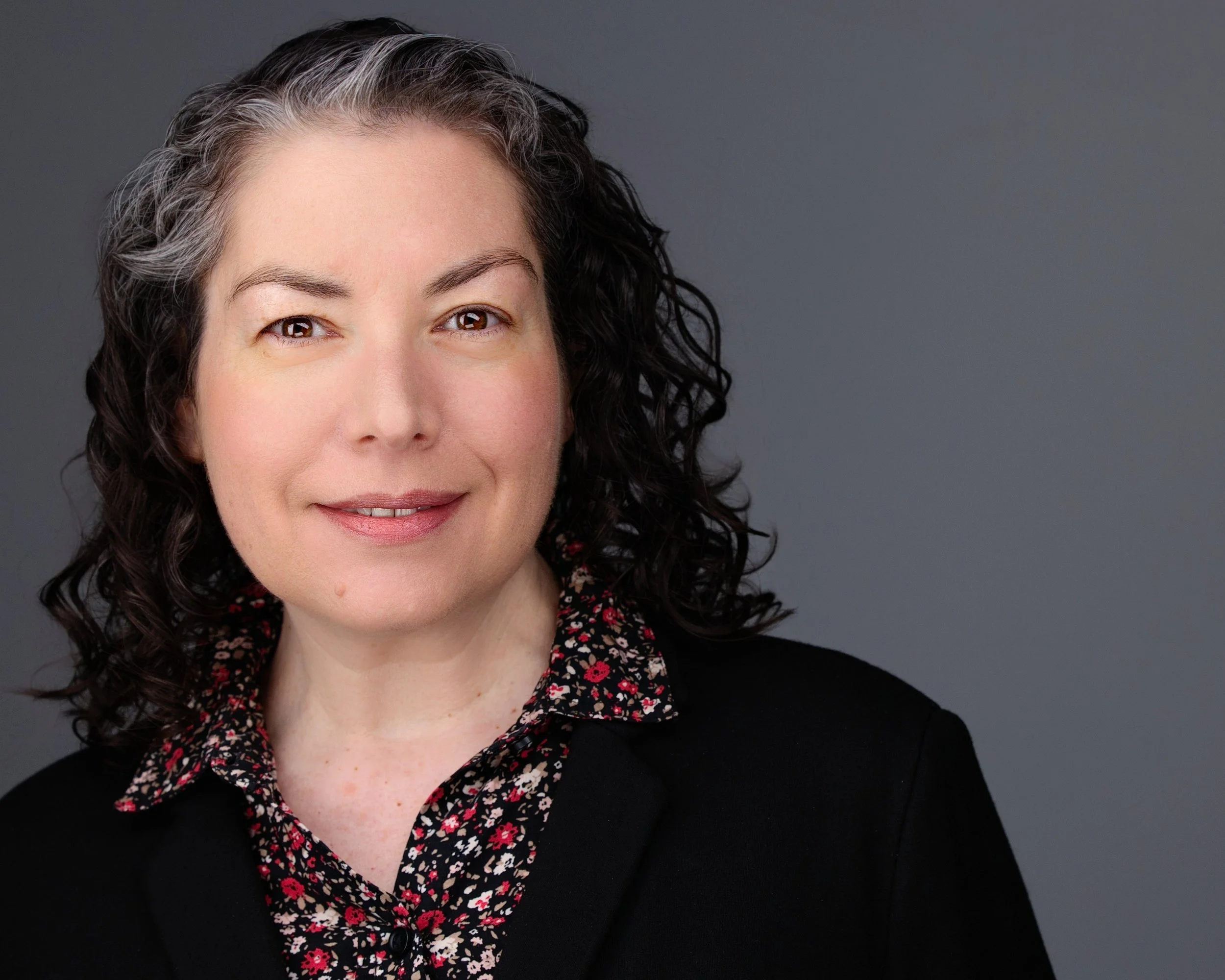Beautiful Woman who is a Seasoned Executive Journalist with long dark hair and a wry smile.