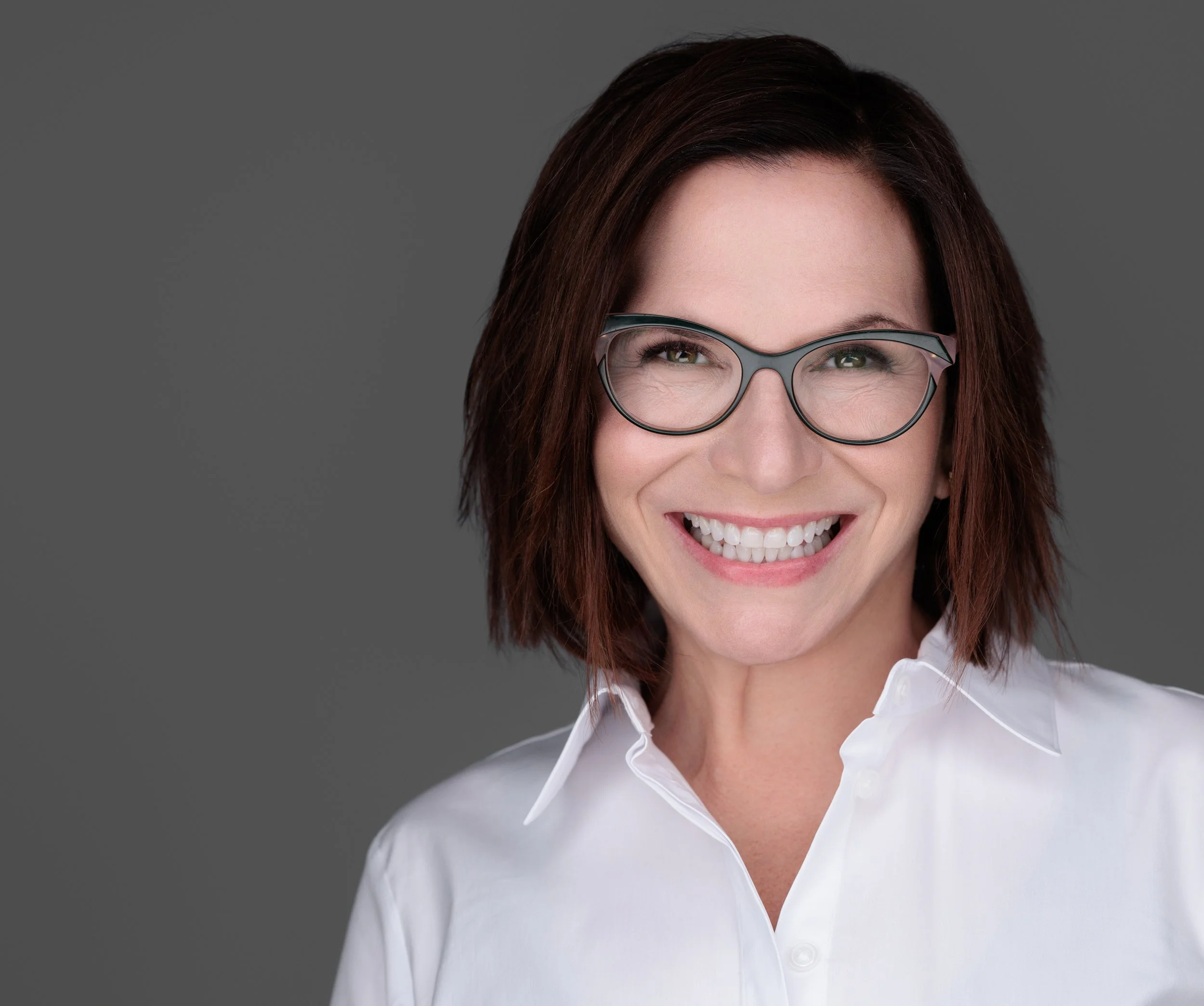 Spectacled woman with dark brown eyes, copper colored hair and a big smile.