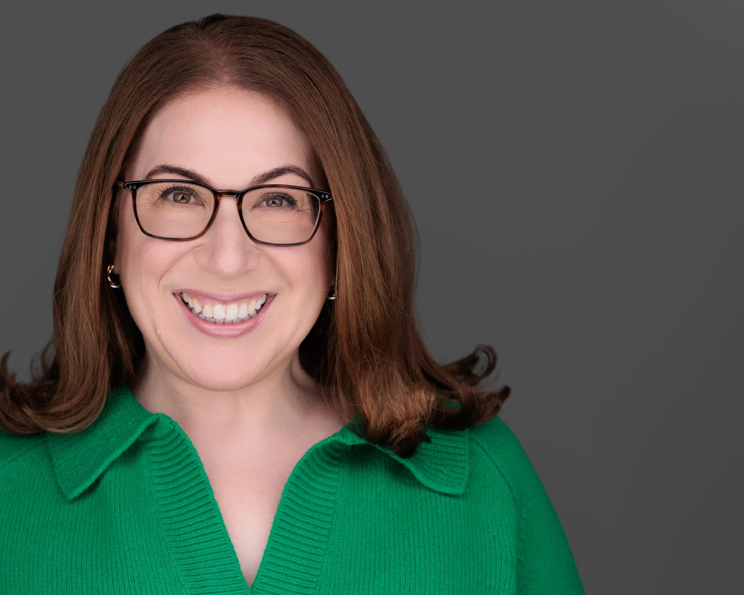 Smiling executive looking woman with kelly green shirt on, glasses and light brown hair.