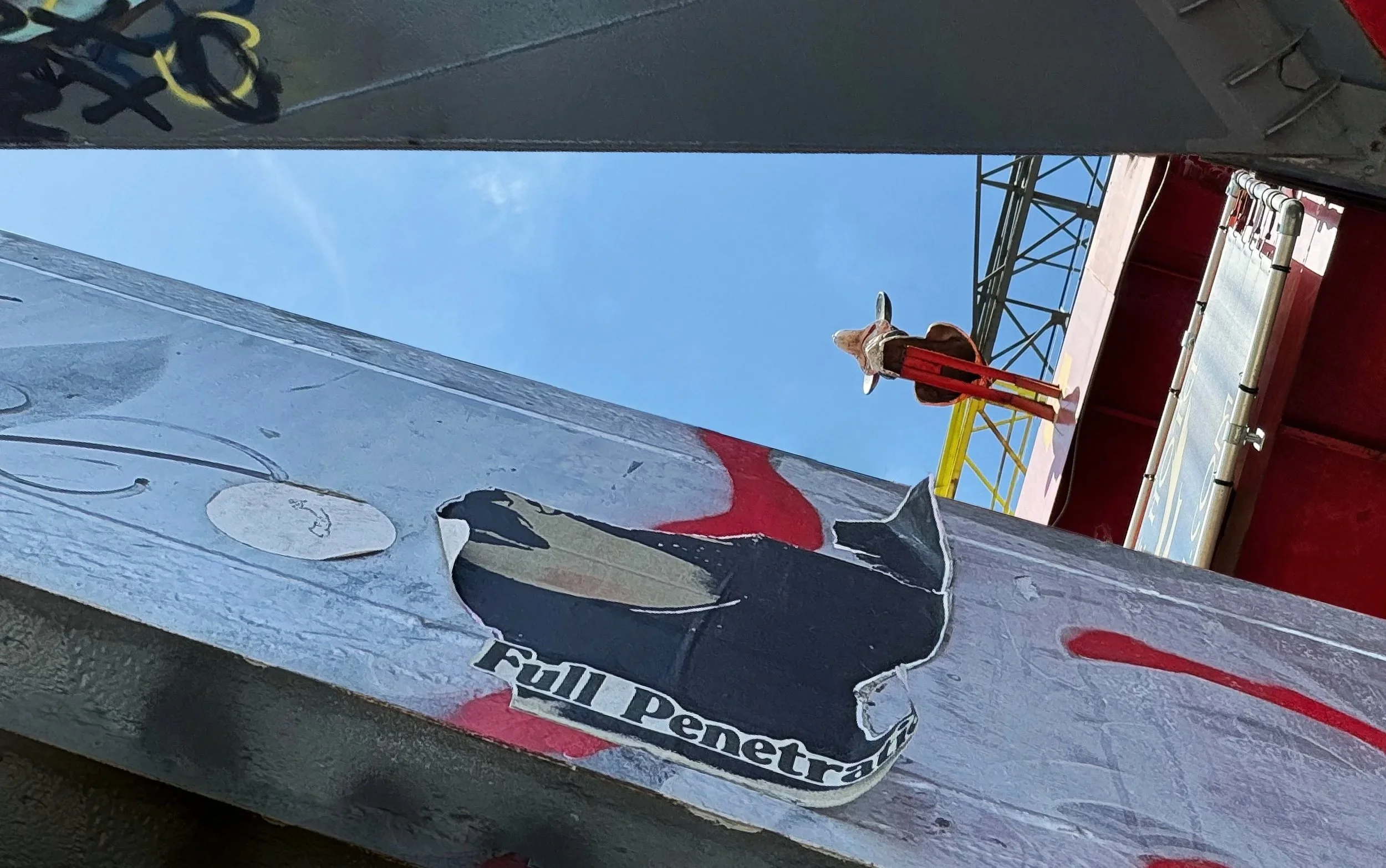 Afbeelding van een skateboard met een afbeelding van een panda op de zijkant, met de tekst 'Felt Penetrra' eronder, gelegen op de rand van een skatebaan. Op de achtergrond is een deel van een constructie en een blauwe lucht zichtbaar.