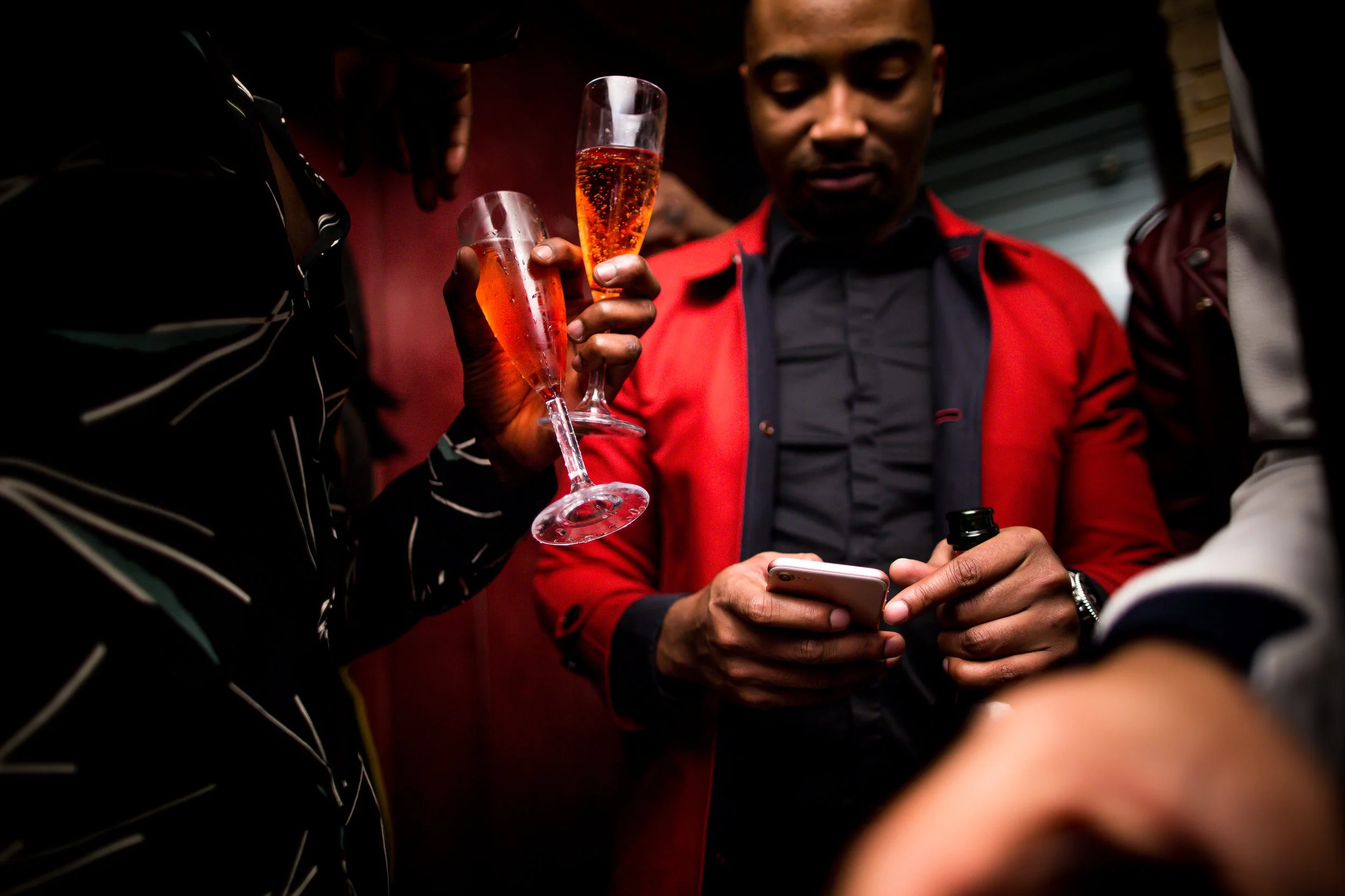 Three people at a social gathering, one holding a phone and the other two holding glasses of sparkling rosé wine.