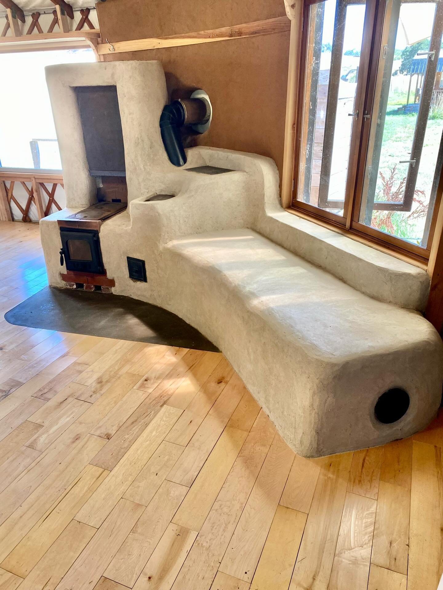 We began constructing our rocket mass heater after insulating the wall behind it and the plywood floor with perlite coated in clay or cement (if it was bearing a heavy load).&nbsp;Then built our firebox (from firebrick), adding a cooktop from an old 