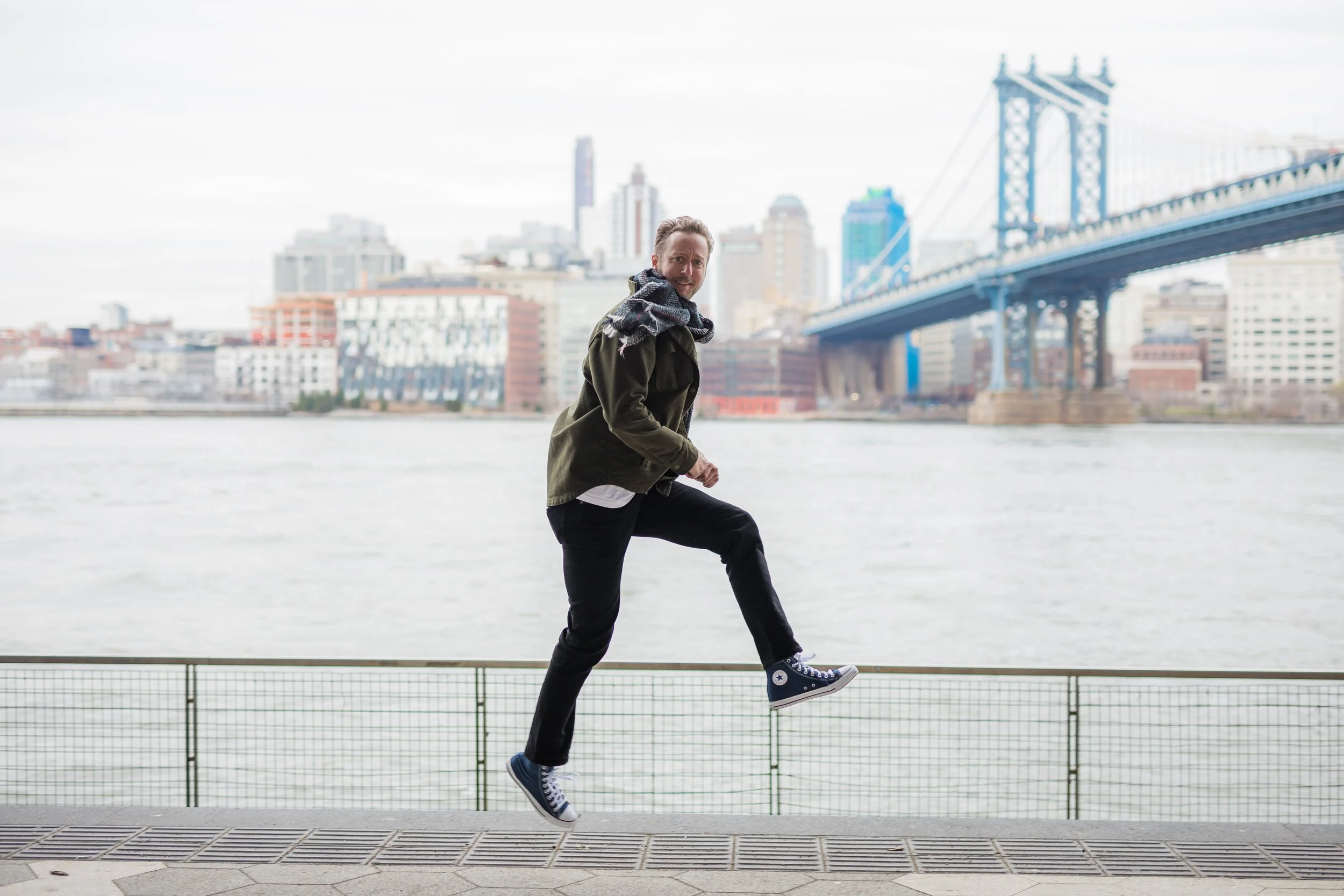 Lifestyle branding portrait of a New York professional leaping along the East River with the Manhattan Bridge behind him, by Blue Sky's Studio