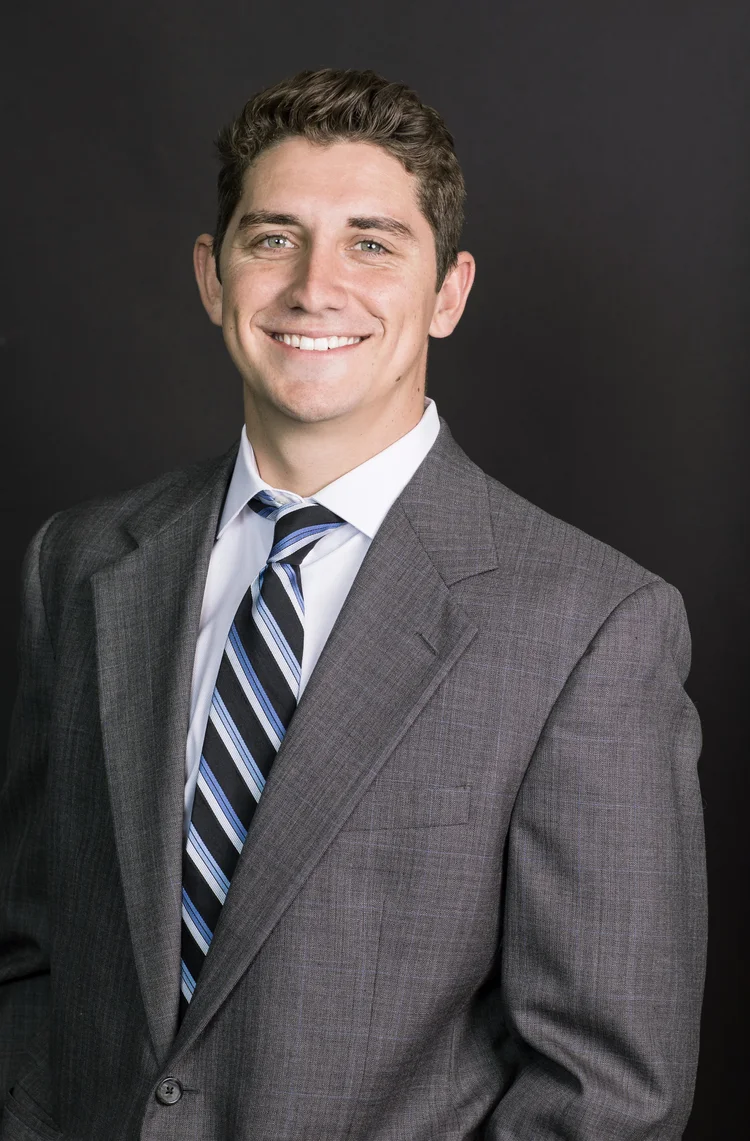Studio headshot of a young executive in a grey suit and striped tie on a dark background
