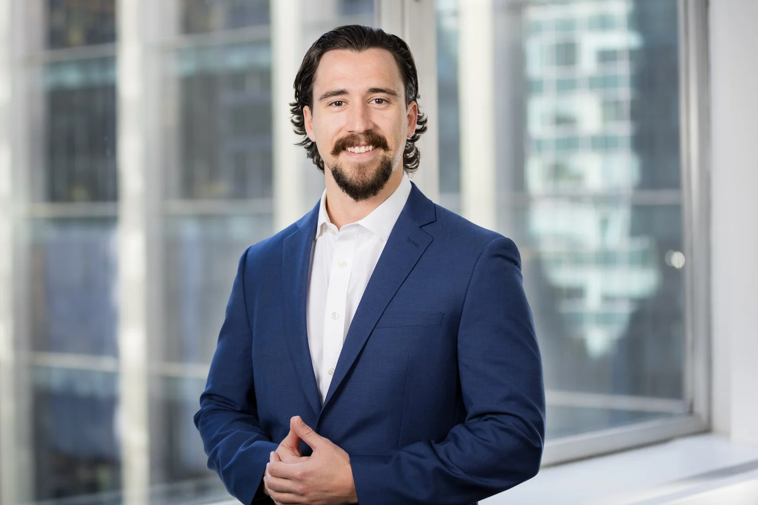 Corporate headshot of a New York executive in a navy suit in front of office windows, photographed on-site by Blue Sky's Studio