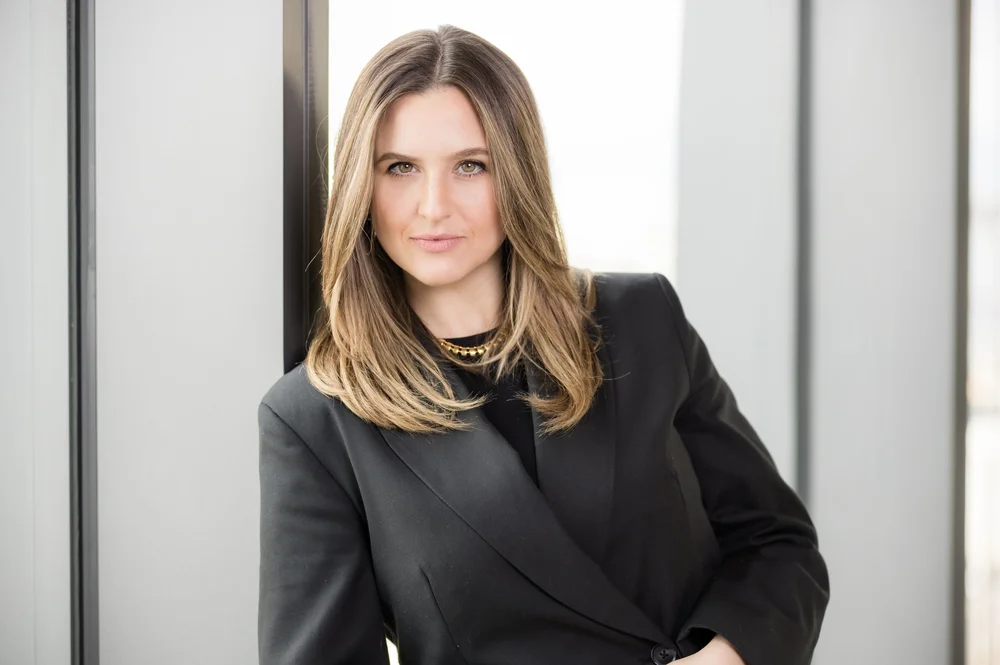 Confident executive portrait of a woman in a black blazer by an office window