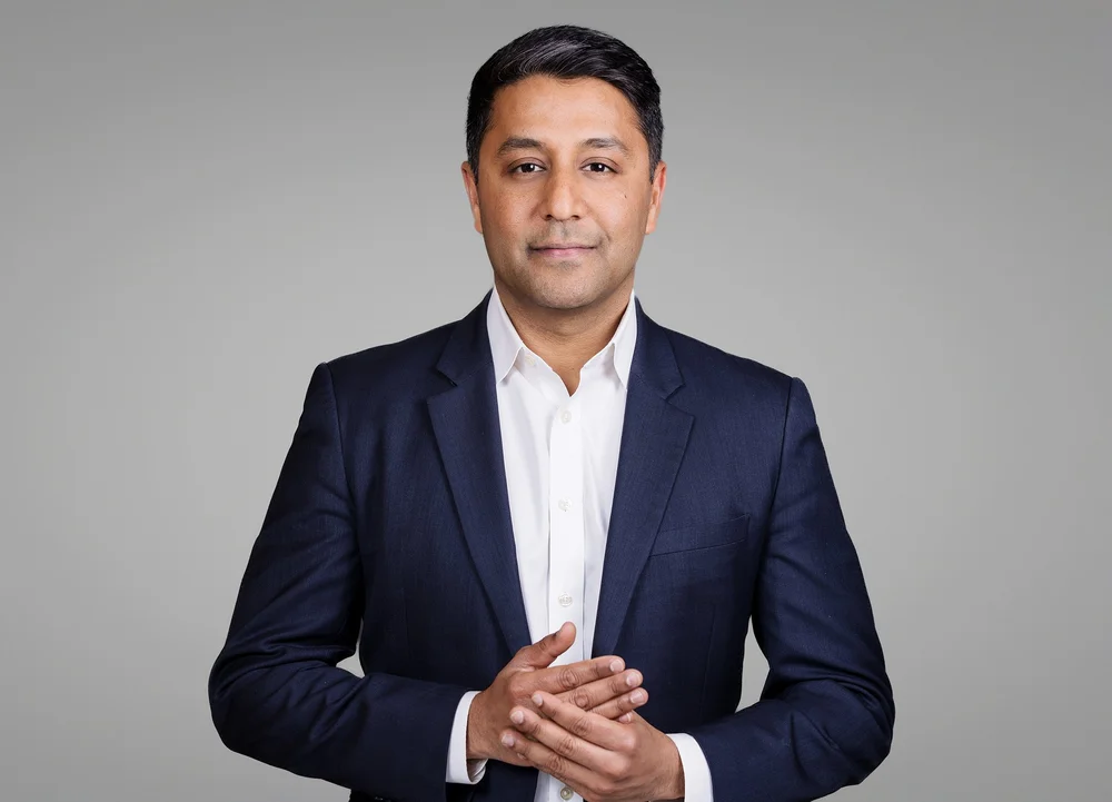 Modern executive headshot of a New York professional in a navy blazer on a grey backdrop, by Blue Sky's Studio