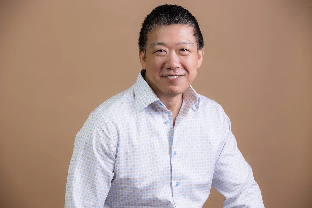 Professional consultant headshot of a man in a light patterned shirt on a beige background