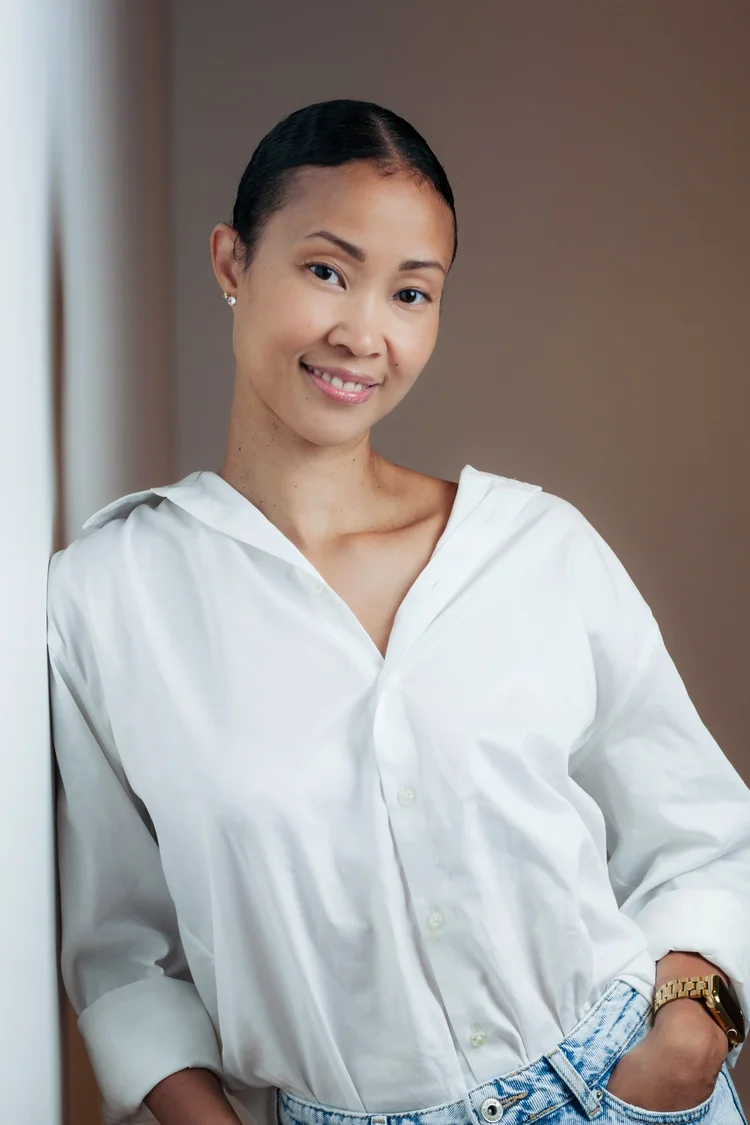 Creative headshot of a woman in a white shirt with her hair pulled back on a warm brown background