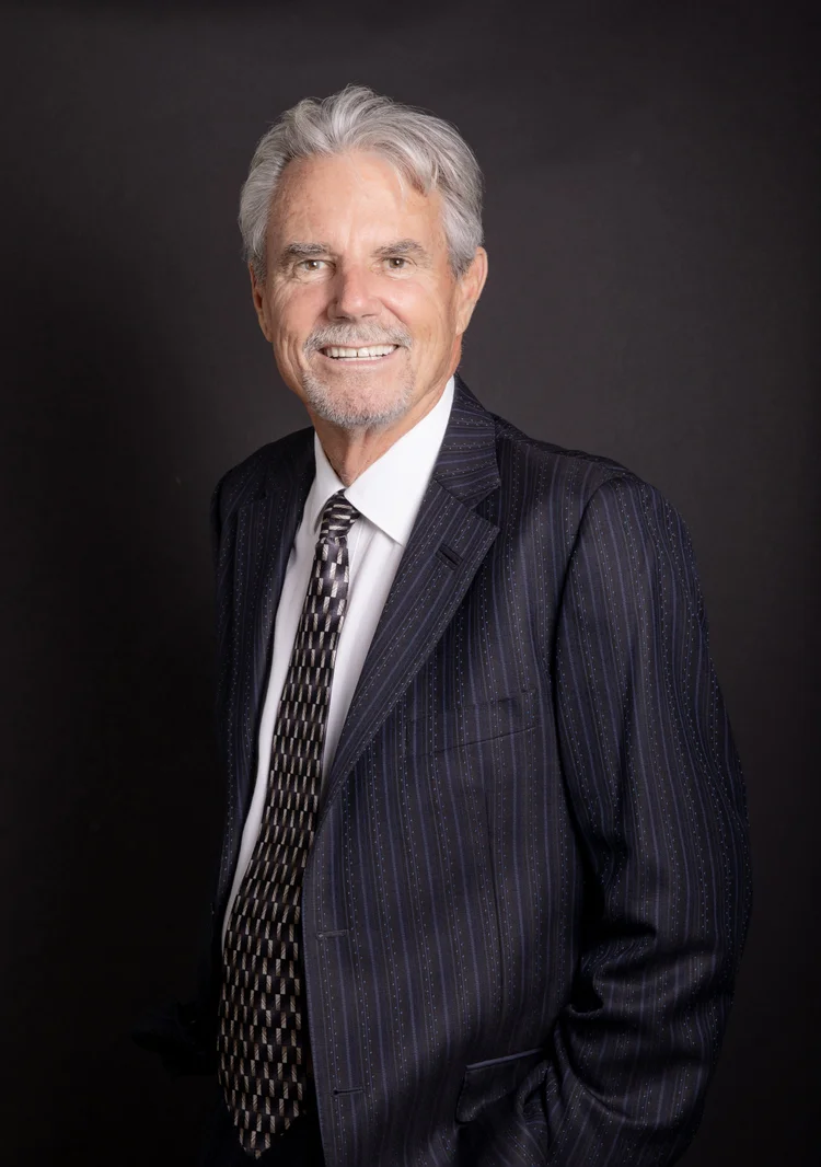 Studio headshot of a silver-haired executive in a pinstripe suit on a dark background