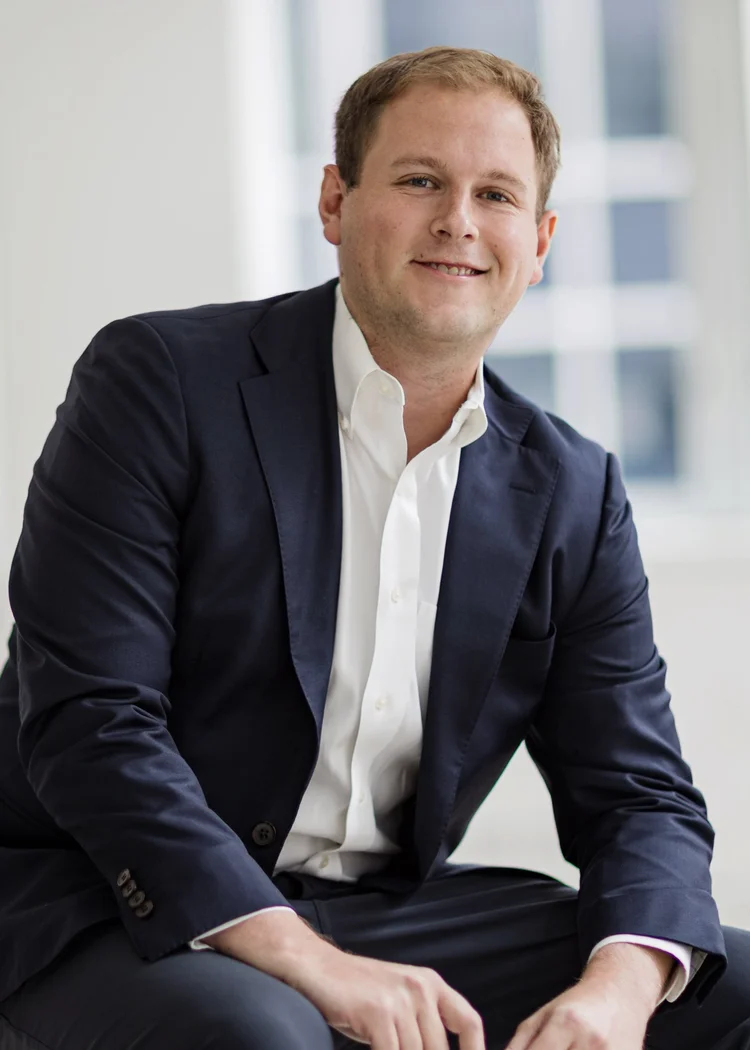 Relaxed seated headshot of a young executive in a navy blazer in a modern office