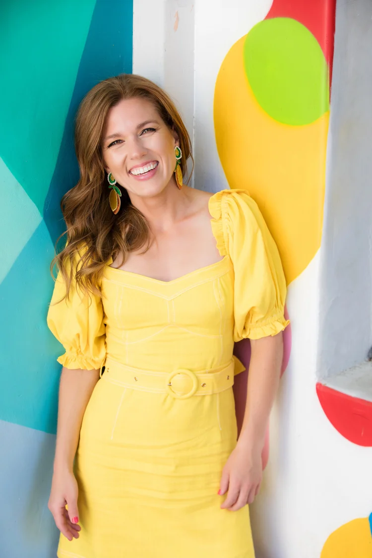 Colorful personal branding portrait of a woman in a yellow dress against a painted mural