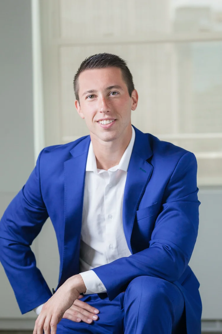 Young executive headshot of a man in a bright blue suit seated in a white office