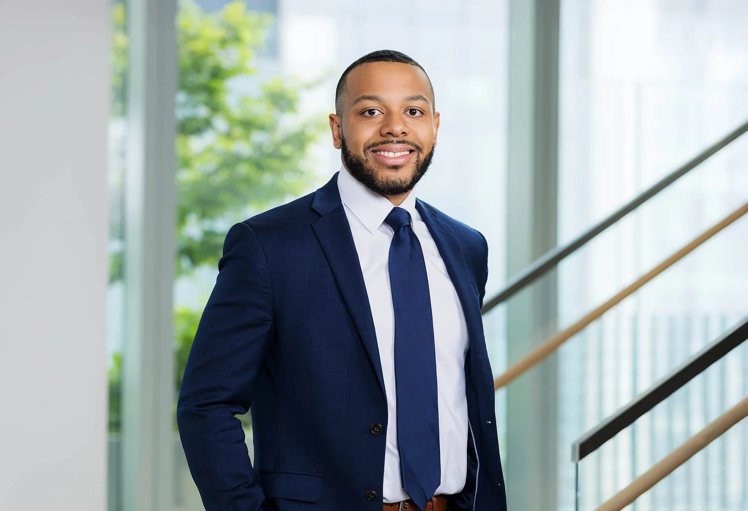 Law firm headshot of a Black attorney in a navy suit and tie by a window in a New York office