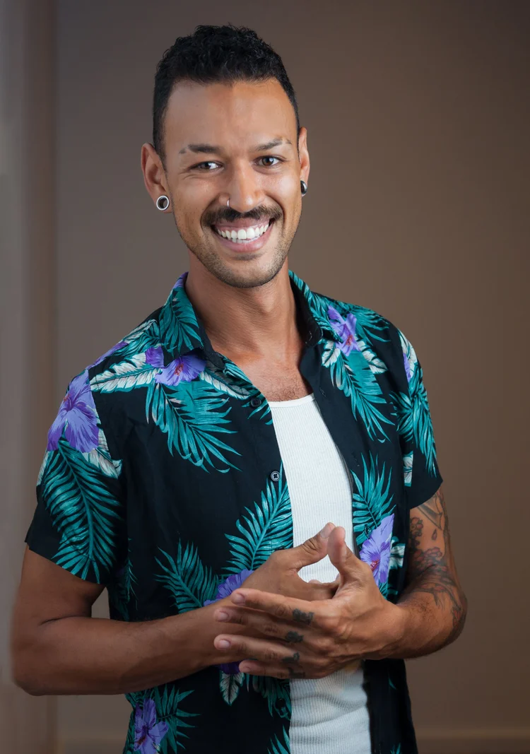 Creative professional headshot of a smiling man with tattoos in a patterned shirt on a brown background