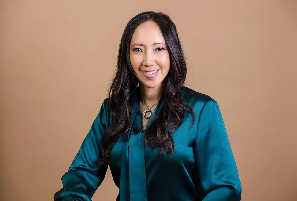 Headshot of a female consultant in a teal satin blouse on a warm beige background