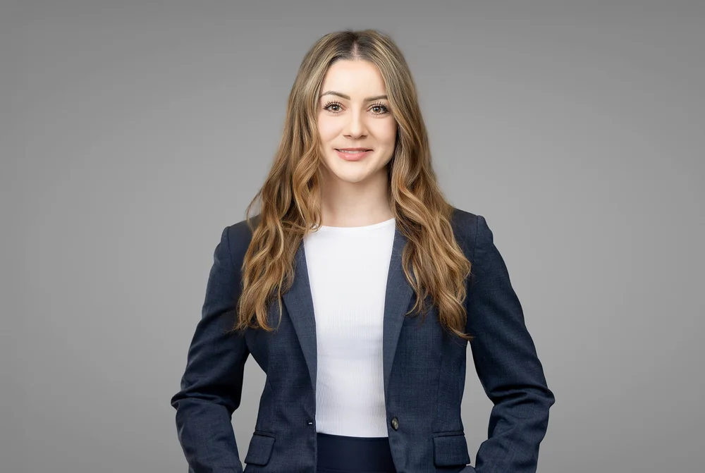 Professional headshot of a female attorney in a navy blazer against a neutral grey backdrop