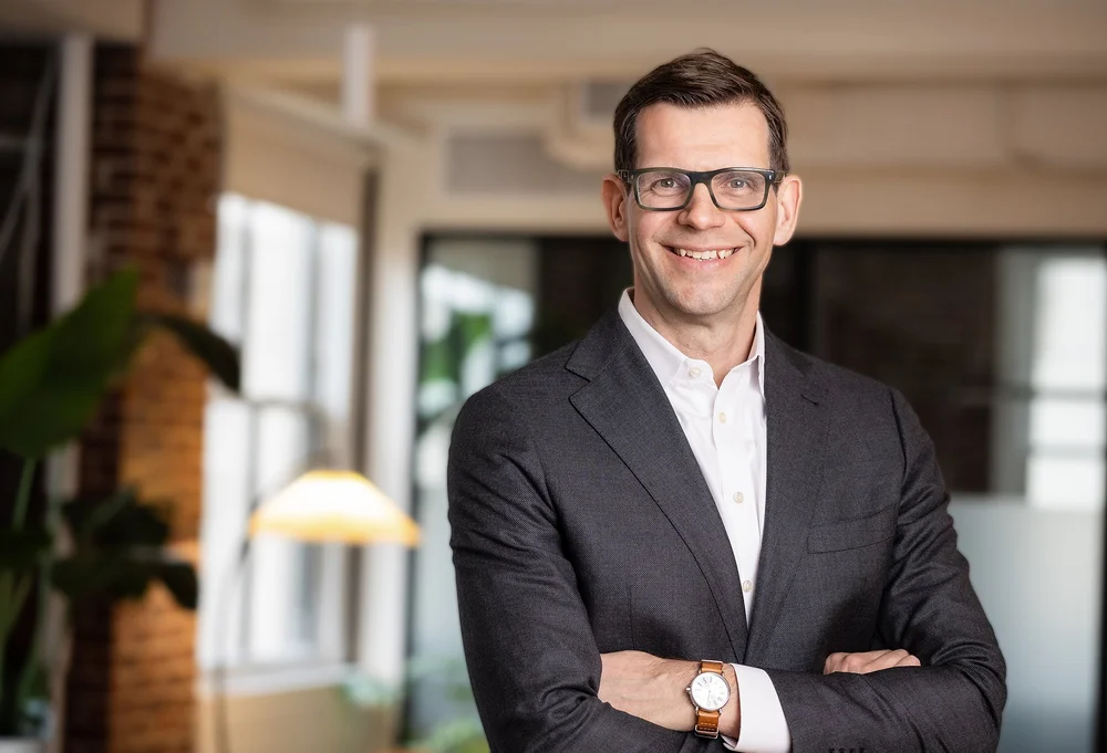 Executive tenant portrait of a smiling man in glasses with arms crossed in a Rockefeller Center office