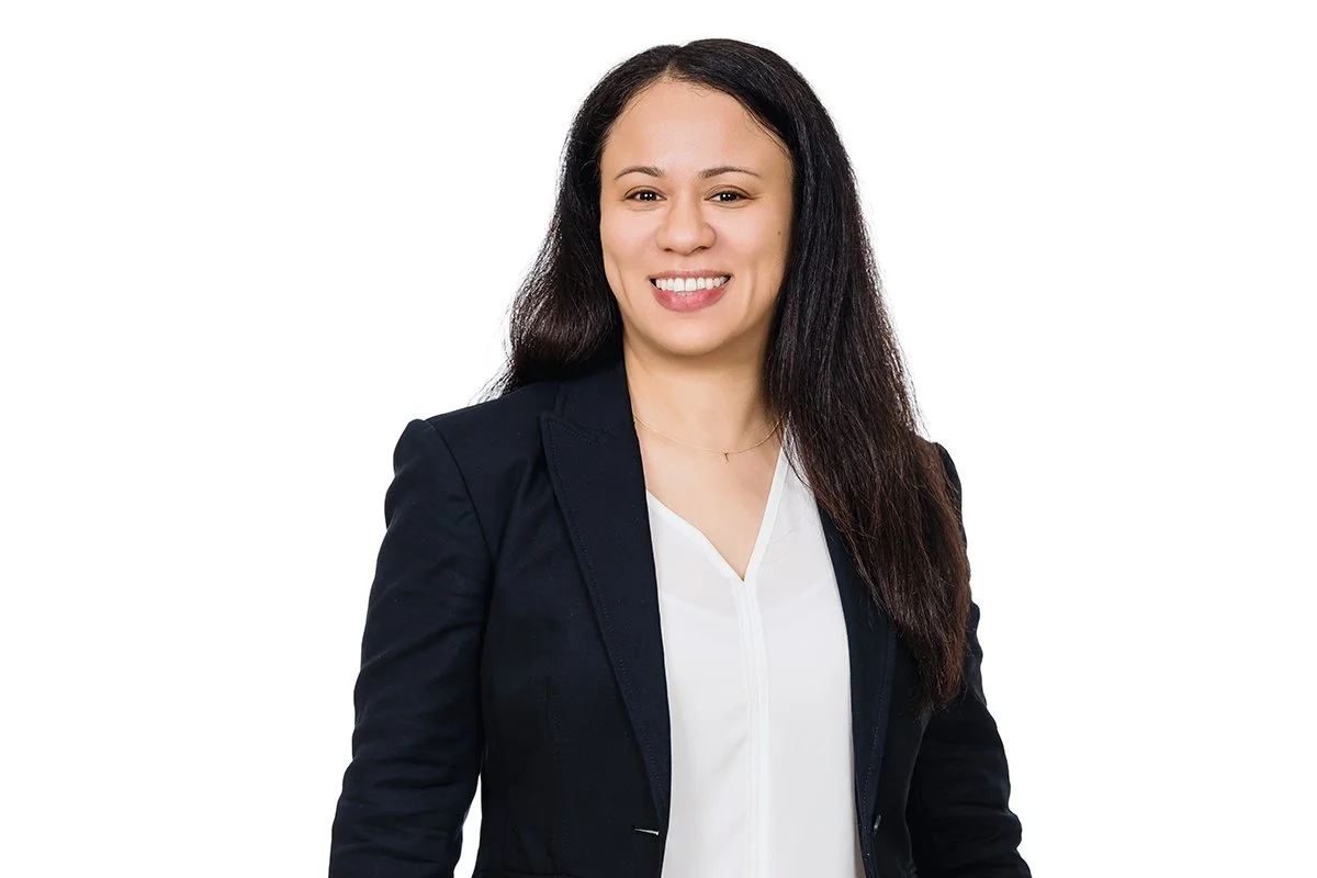 Professional woman with long dark hair smiling, wearing a black blazer and white blouse, against a white background.