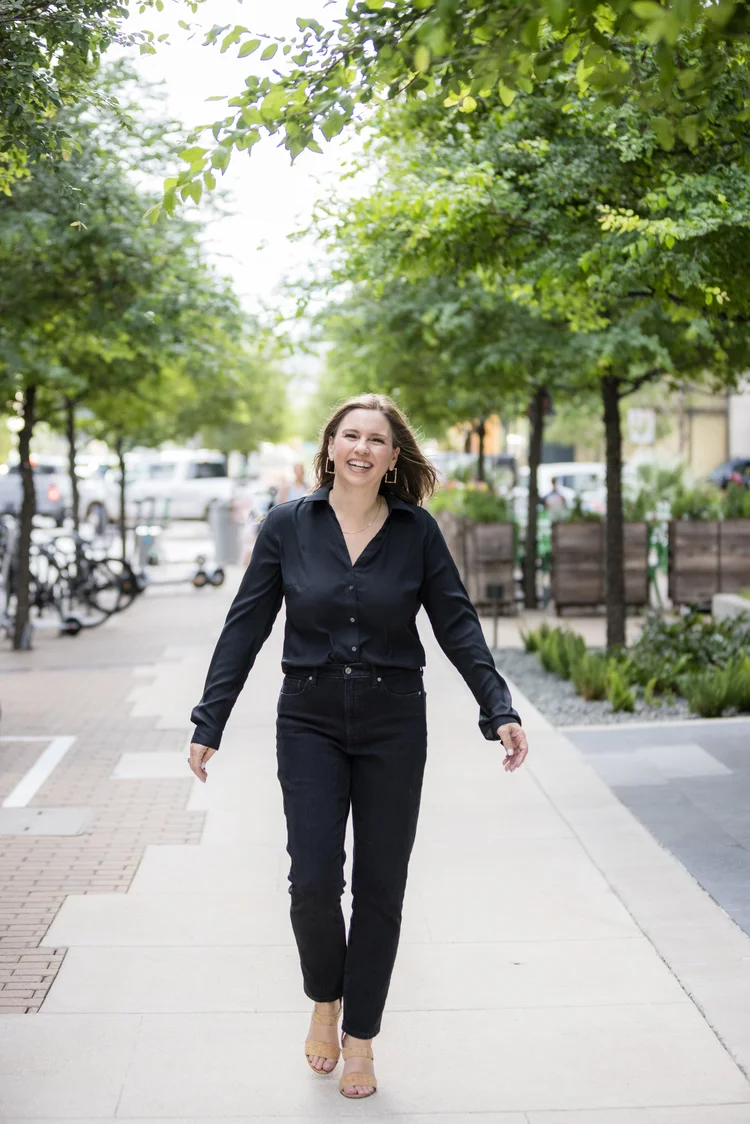 Branding photo of a woman in a black shirt and pants walking down a tree-lined sidewalk