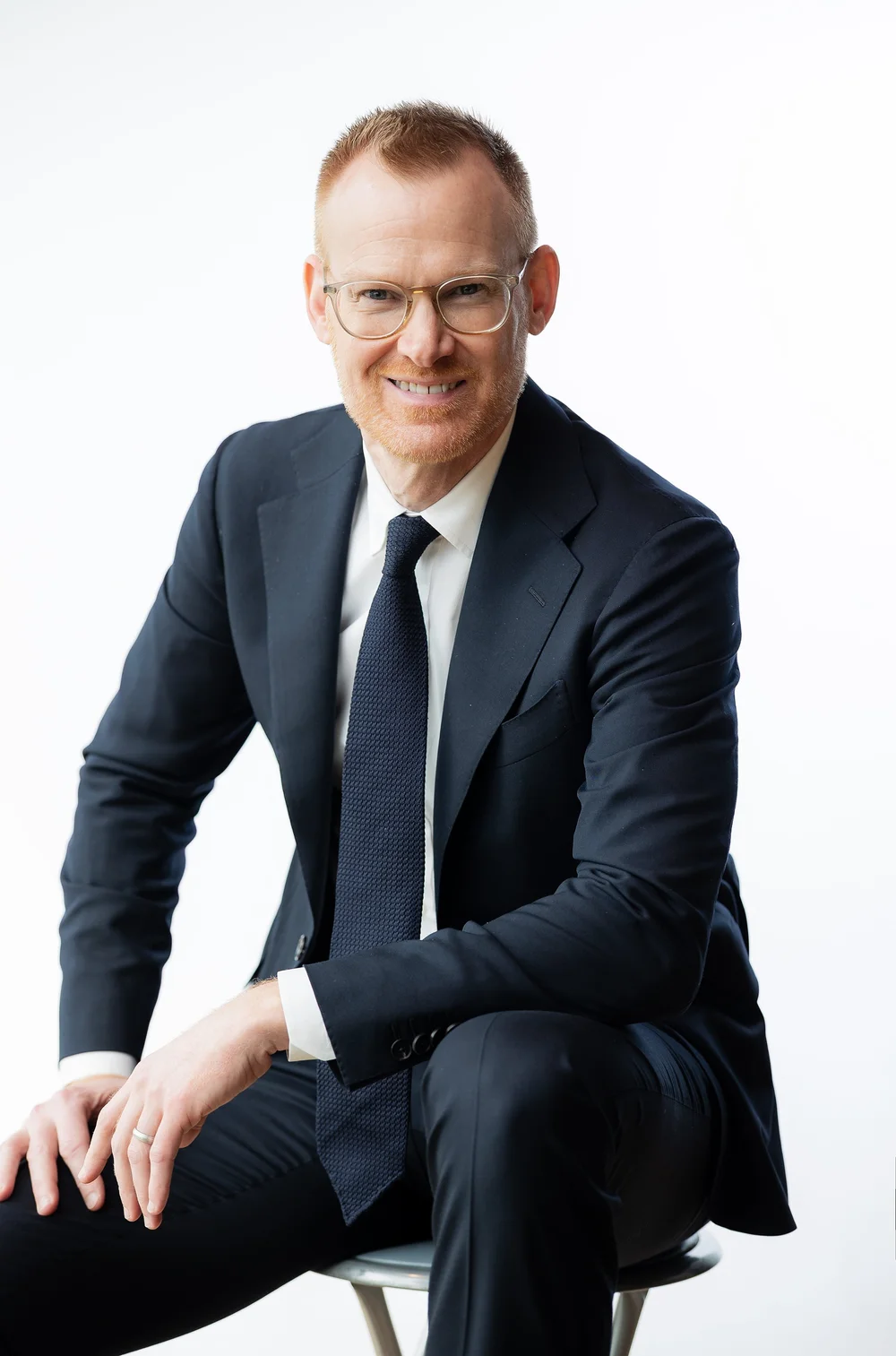 Seated attorney headshot of a man in glasses and a dark suit on a white background