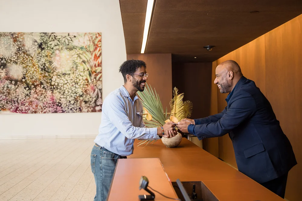 Two men smiling and shaking hands at a wood reception desk in an office lobby