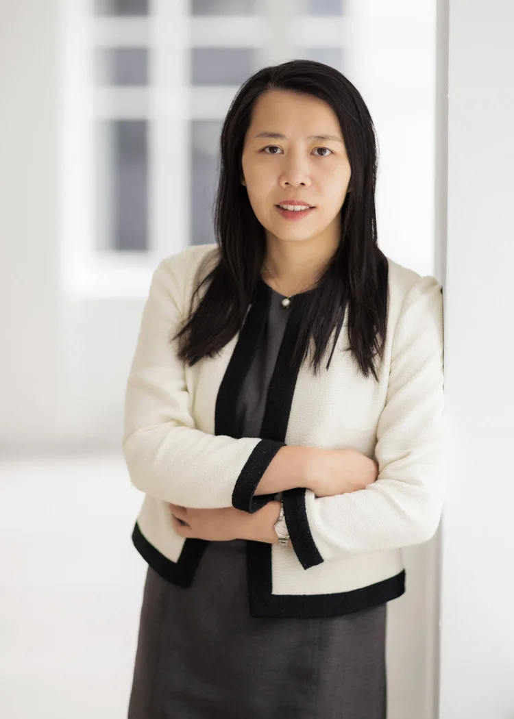 Executive headshot of a woman in a cream and black jacket with arms crossed in a bright office